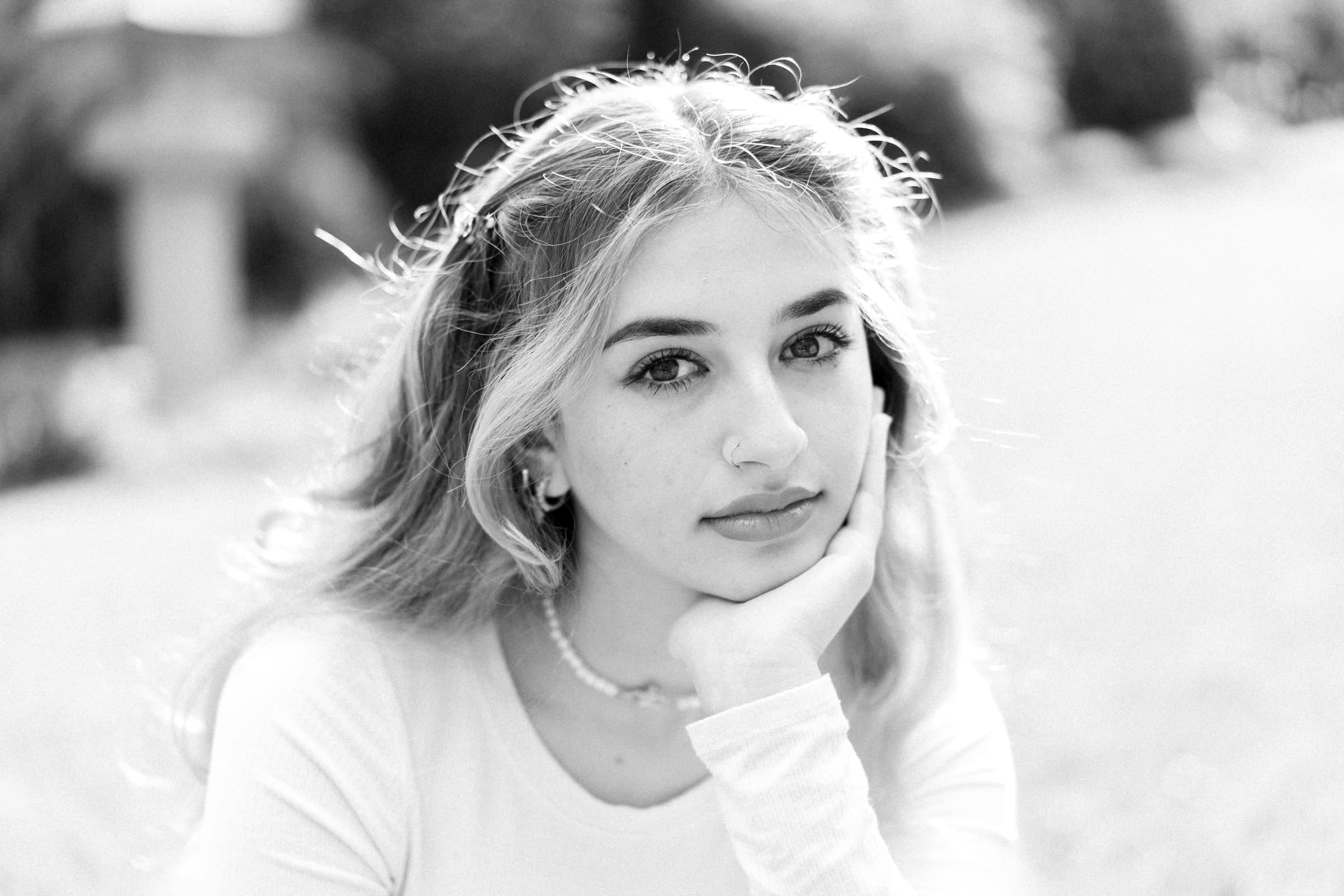 durham portrait photographers - sophia's senior session Black and white portrait of a young person with long hair, resting their chin on their hand, captured beautifully by a Durham portrait photographer. They look directly at the camera, set against a softly blurred background that creates a serene atmosphere.