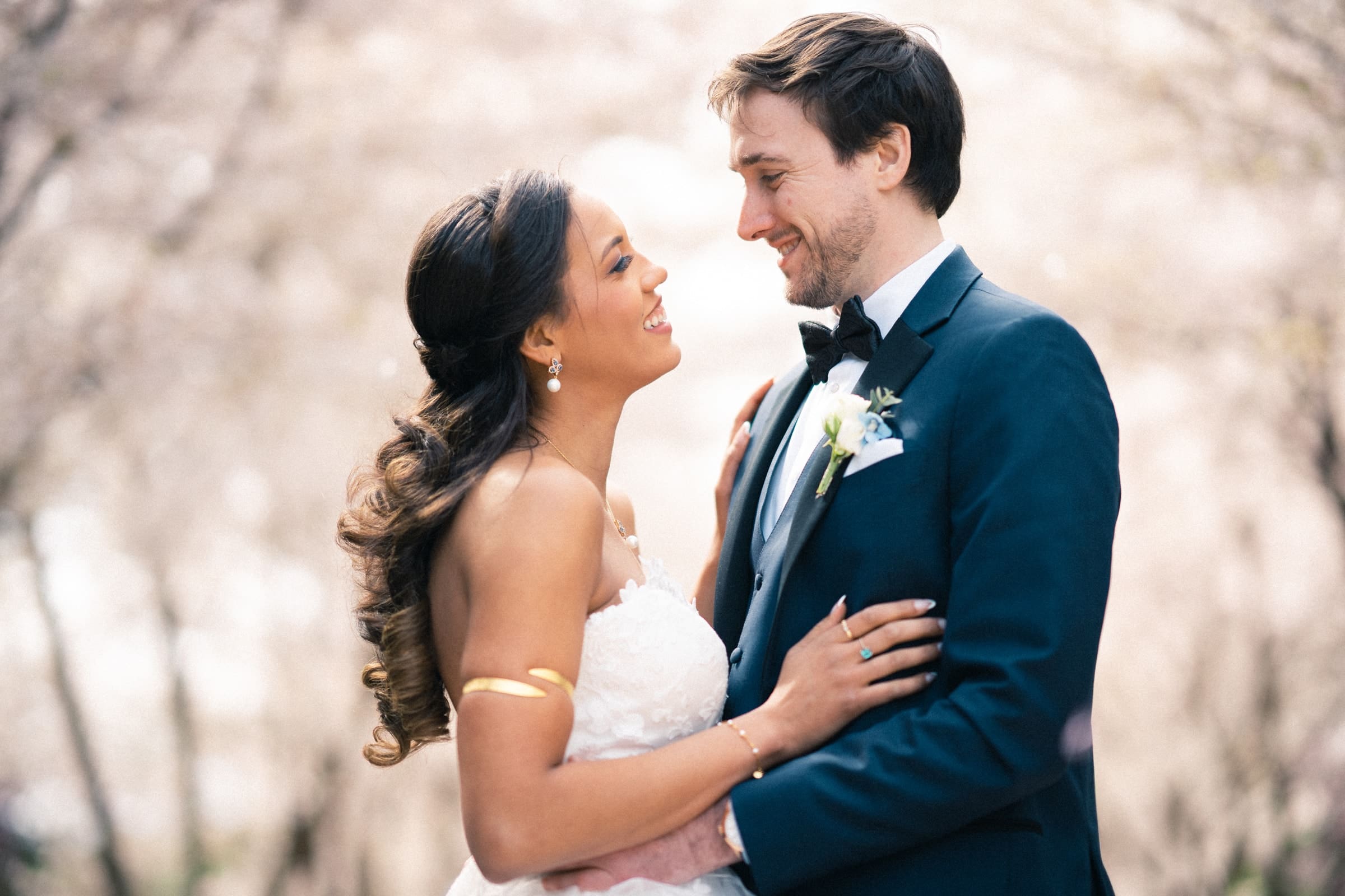 duke chapel & cookery wedding - sasha & ben A bride and groom stand close, gazing lovingly into each other's eyes against a backdrop of soft, blurred cherry blossoms at the iconic Duke Chapel. The bride wears a white gown, and the groom is in a dark suit with a white boutonnière.