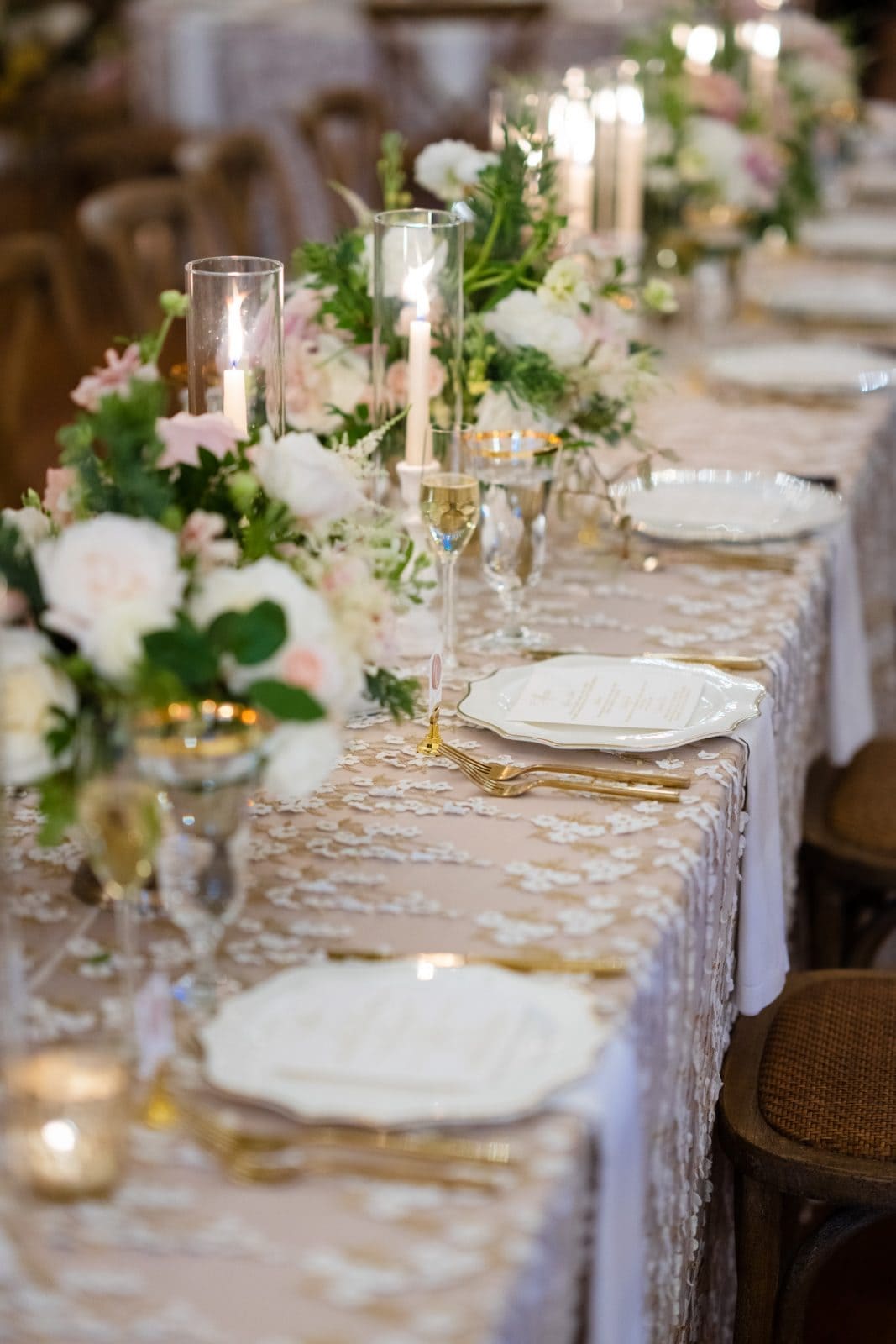 historic wakefield barn wedding photography - jennifer & stefan A beautifully set wedding table at Wakefield Barn exudes elegance with floral arrangements and lit candles. Lace tablecloths, gold-rimmed plates, and crystal glassware enhance the romantic and sophisticated ambiance, perfect for capturing exquisite wedding photography.