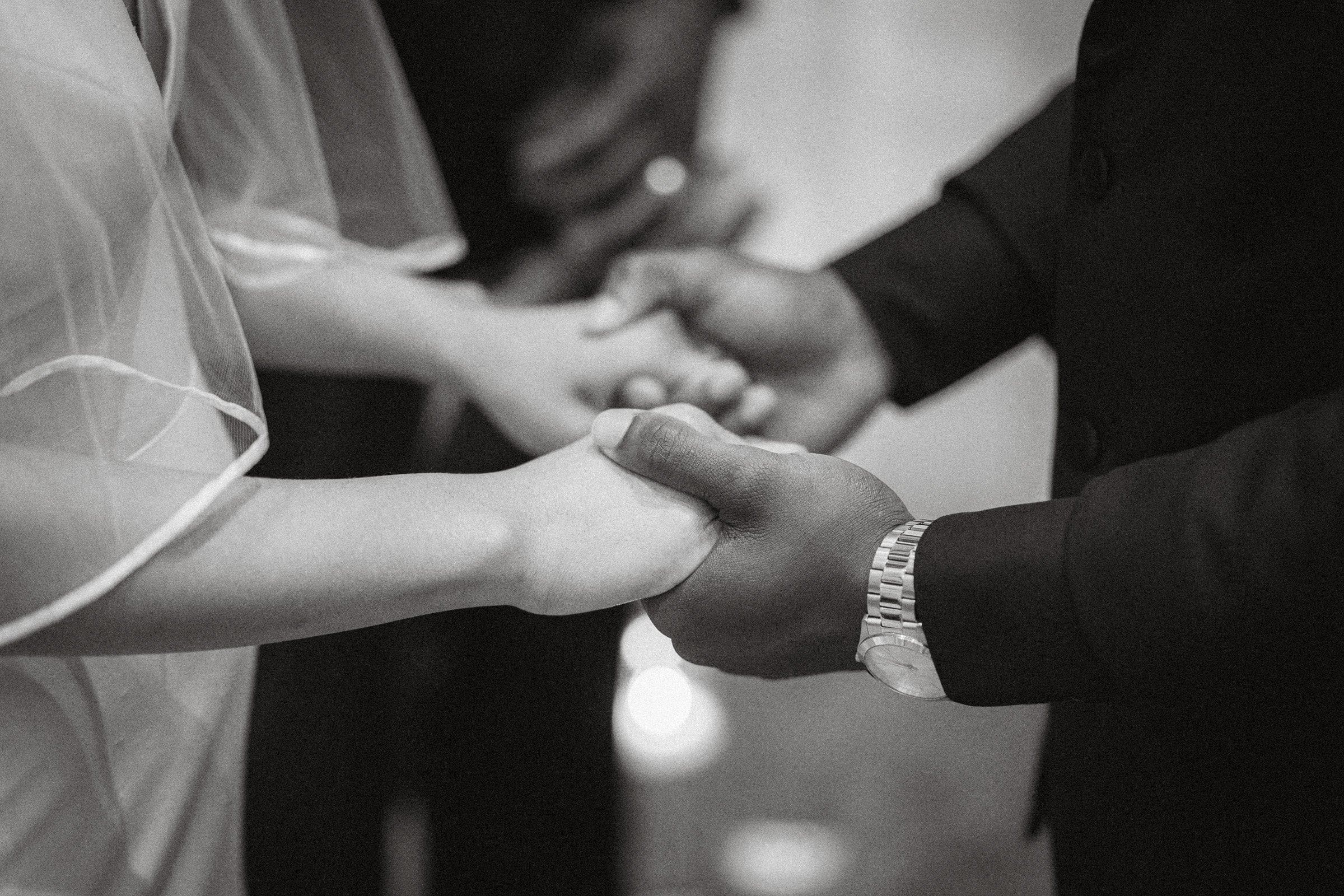 umstead wedding photography - kayla & deandre In a black and white image, a couple holds hands at an Umstead wedding. One person is wearing a veil, the other a watch. Both are in formal attire, captured in a moment of connection and tenderness.