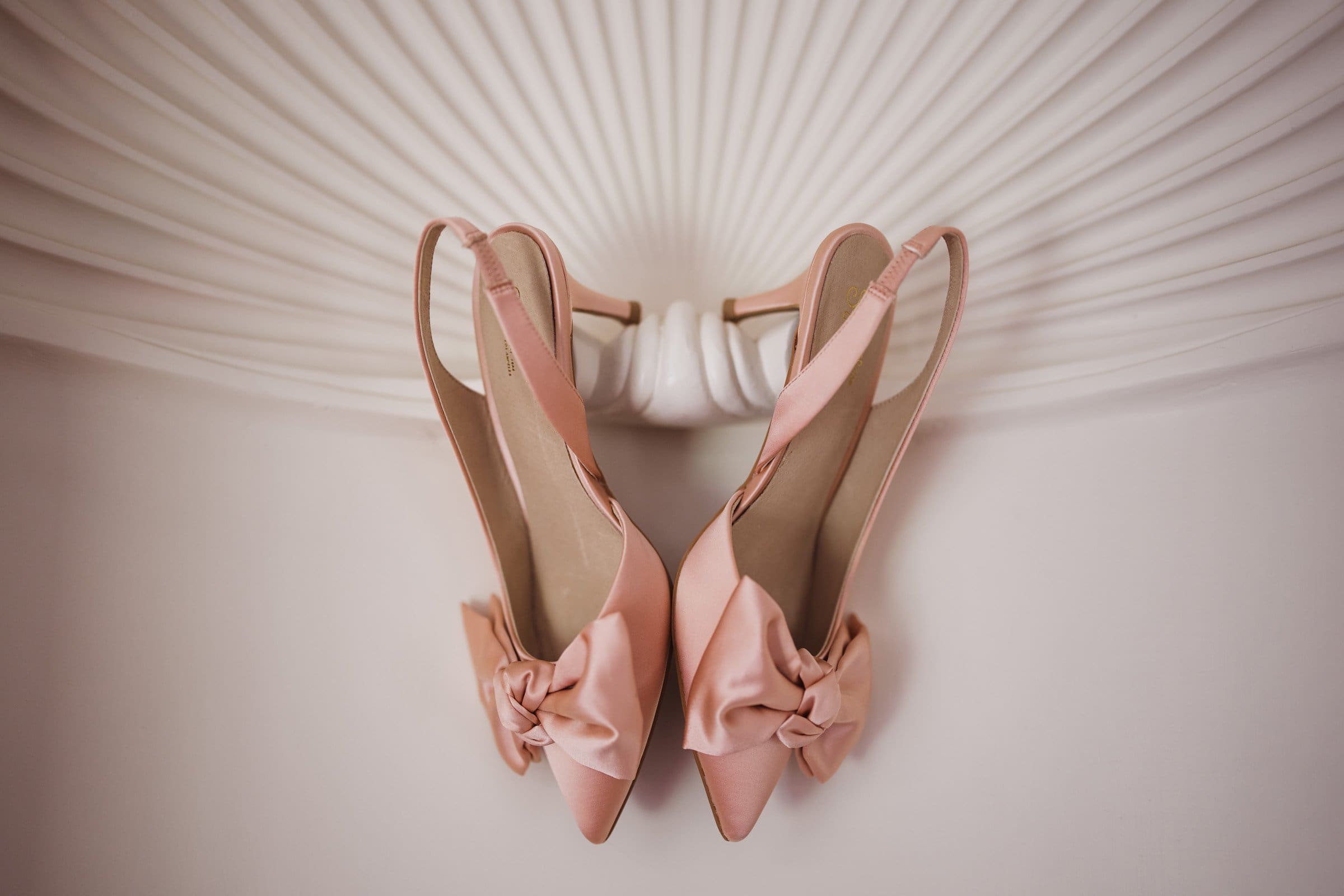 duke gardens wedding photography - ann & tim A pair of elegant pink slingback shoes with bows are positioned upside down, set against a textured, circular background design—perfectly capturing the charm of Duke Gardens wedding photography.