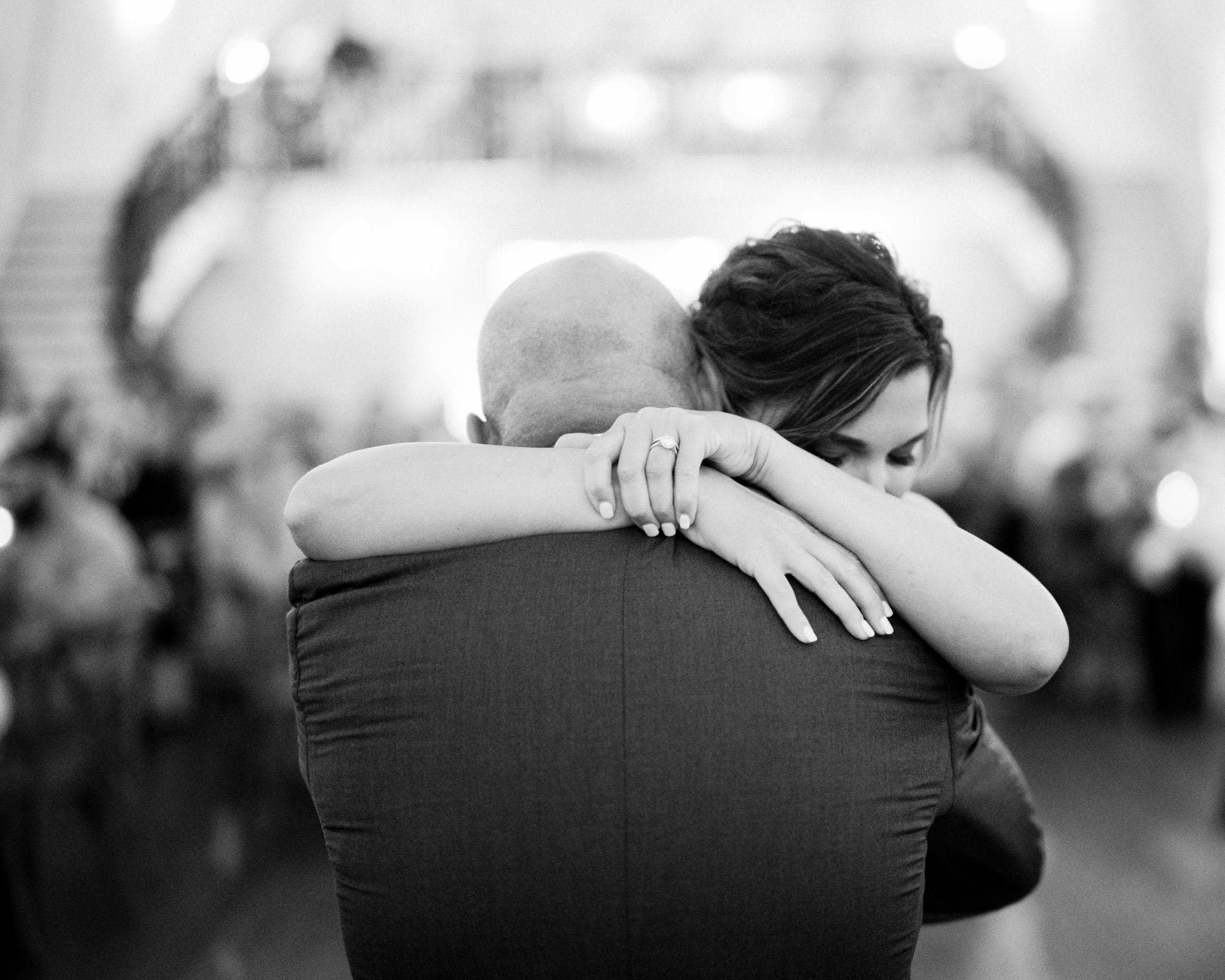 historic wakefield barn wedding - logan & rhett A black and white photo captures a couple embracing closely, the woman's arms lovingly wrapped around the man's neck as she rests her head on his shoulder. The softly blurred background hints at an intimate setting, perhaps a memorable Wakefield Barn wedding.