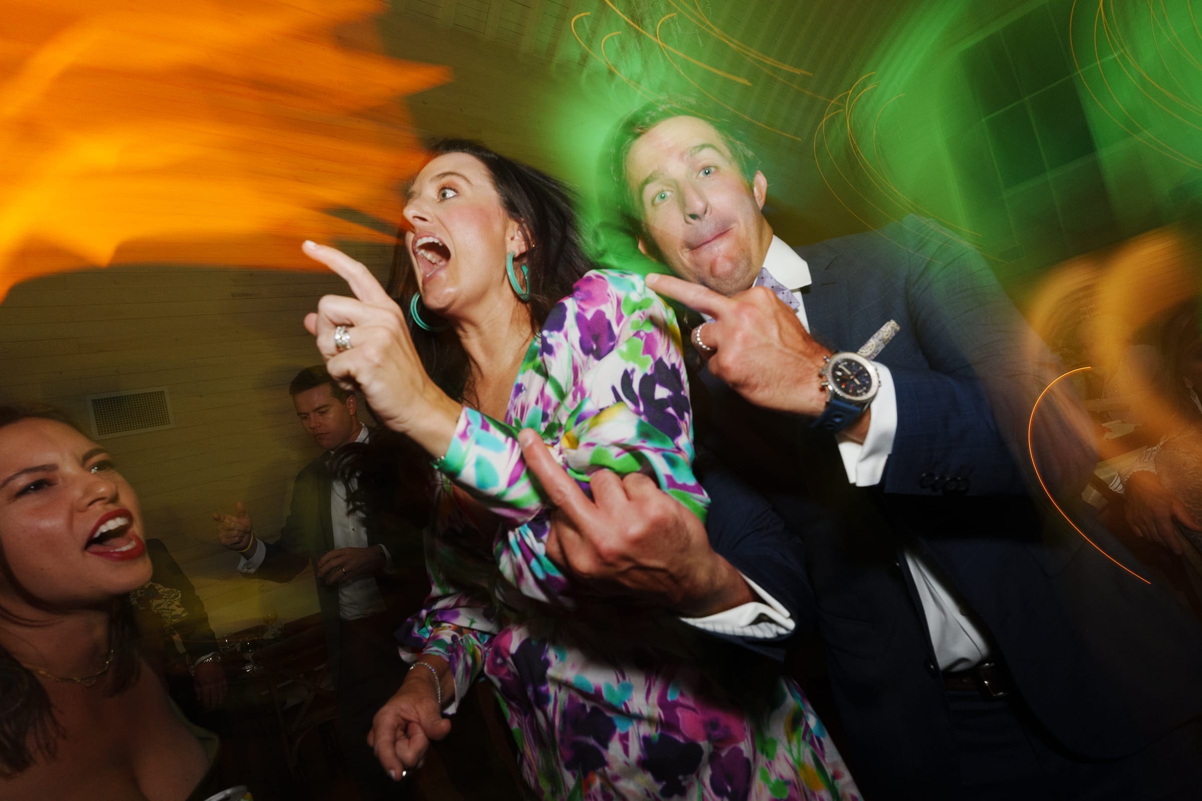 historic wakefield barn wedding - logan & rhett At a lively Wakefield Barn wedding, a group of people energetically dance under colorful swirling lights. Two individuals prominently gesture with their hands, adding to the joy and animated atmosphere that fills the party.