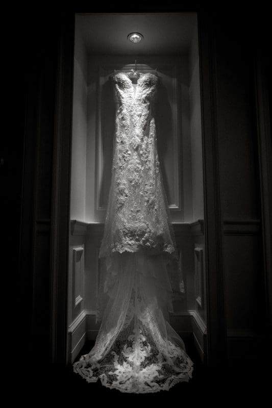 A vintage-style lace wedding dress elegantly showcased in a softly lit niche, reminiscent of a Duke Gardens wedding, highlighting its intricate patterns and timeless design.