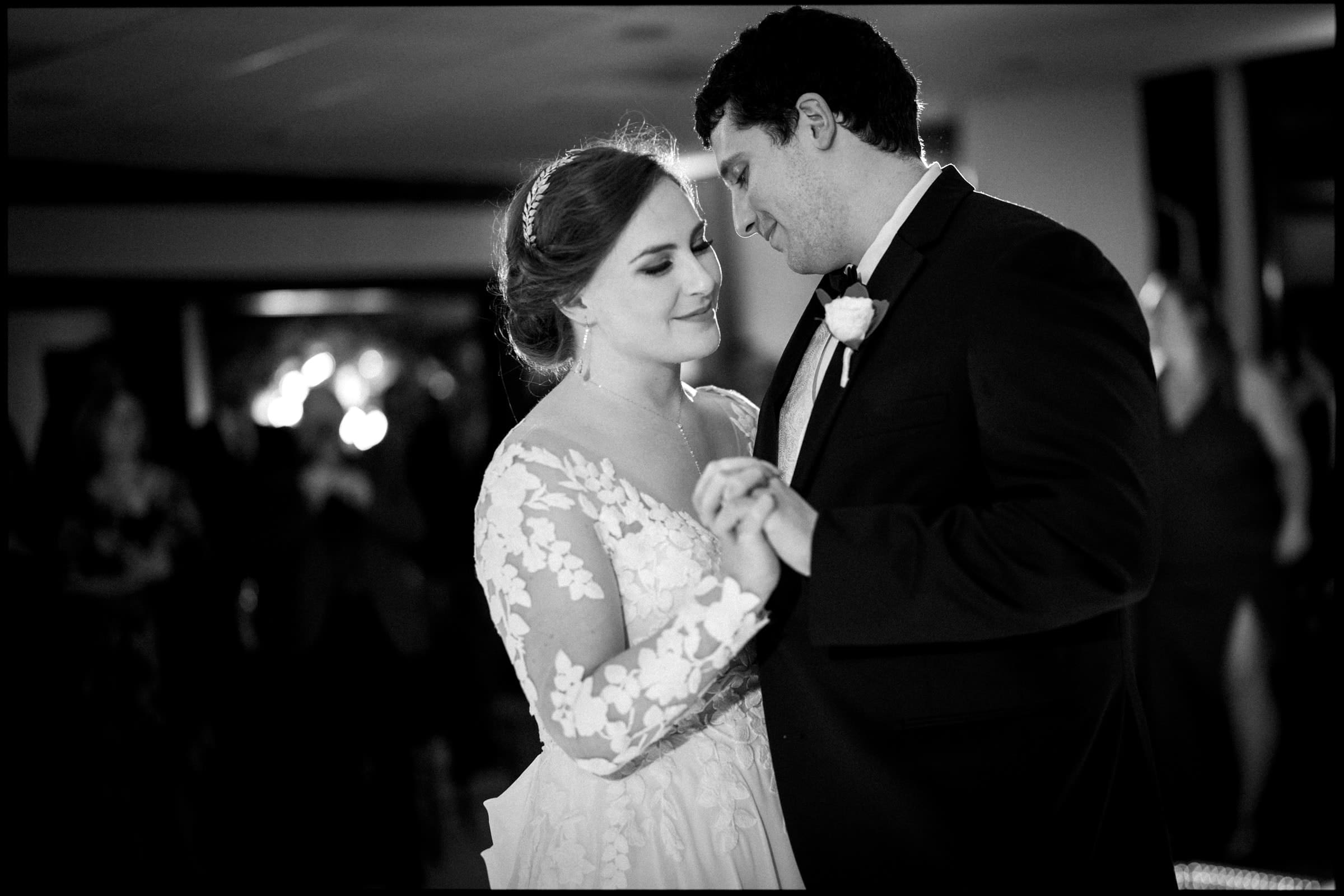 A bride and groom share a tender moment during their first dance at their Duke Chapel wedding. The bride glows in a lace dress, while the groom stands in a dark suit with a boutonniere. The softly blurred background beautifully highlights the couple's intimacy.