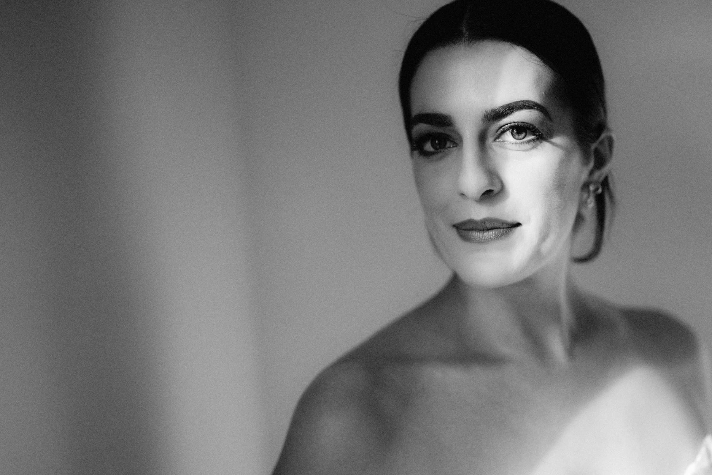 Black and white portrait of a person with dark hair pulled back, looking at the camera. Soft shadows and lighting create a serene atmosphere, reminiscent of a Melrose Knitting Mill wedding backdrop.