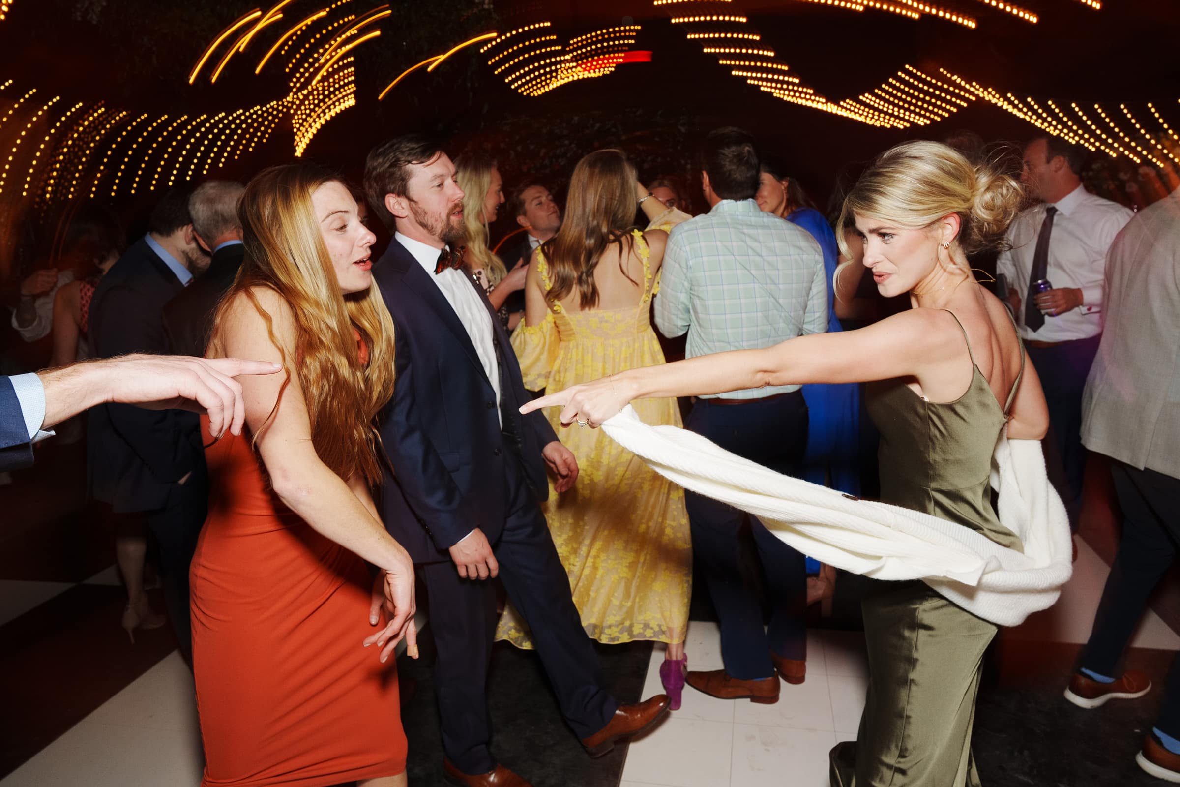 sutherland estate wedding - stephanie & hunter At a Sutherland Estate wedding, people dance joyfully beneath the glow of string lights. A woman in an olive dress points playfully while others mingle and sway to the rhythm in the background.