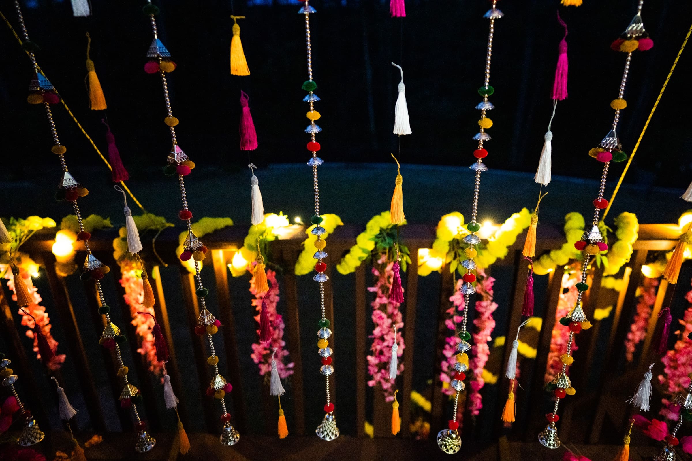 indian wedding photography - rithika & chanakya Hanging festive decorations with colorful tassels and beads, and strings adorned with bright yellow and pink flowers, perfectly complement the soft lighting. The scene captures the enchanting atmosphere ideal for Indian wedding photography, creating a warm and inviting ambiance.