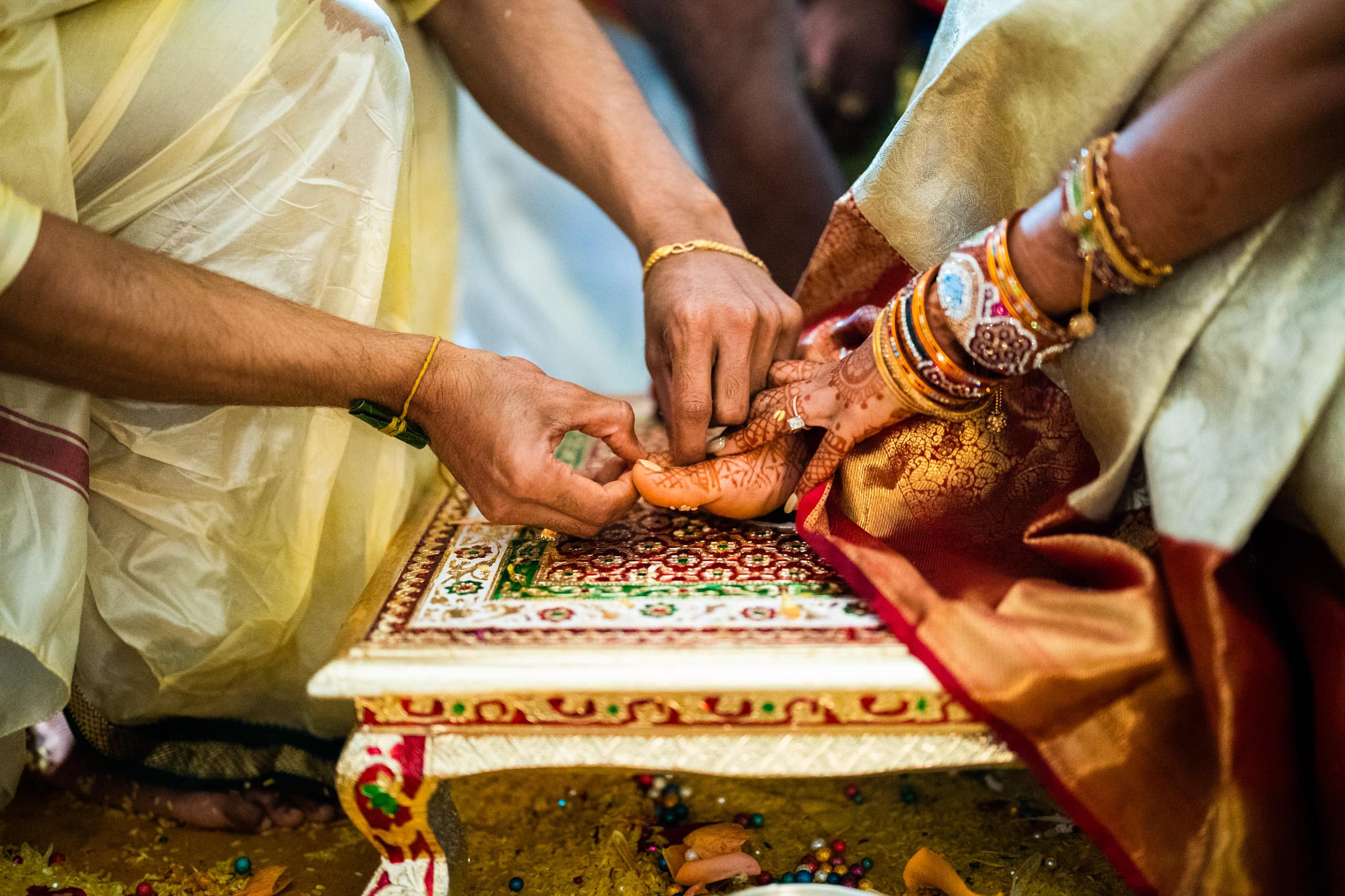 indian wedding photography - rithika & chanakya A traditional Indian wedding ceremony captured in beautiful wedding photography shows the groom touching the bride's henna-adorned feet. She wears gold bangles as they sit on an intricately decorated platform, perfectly preserving this timeless moment.