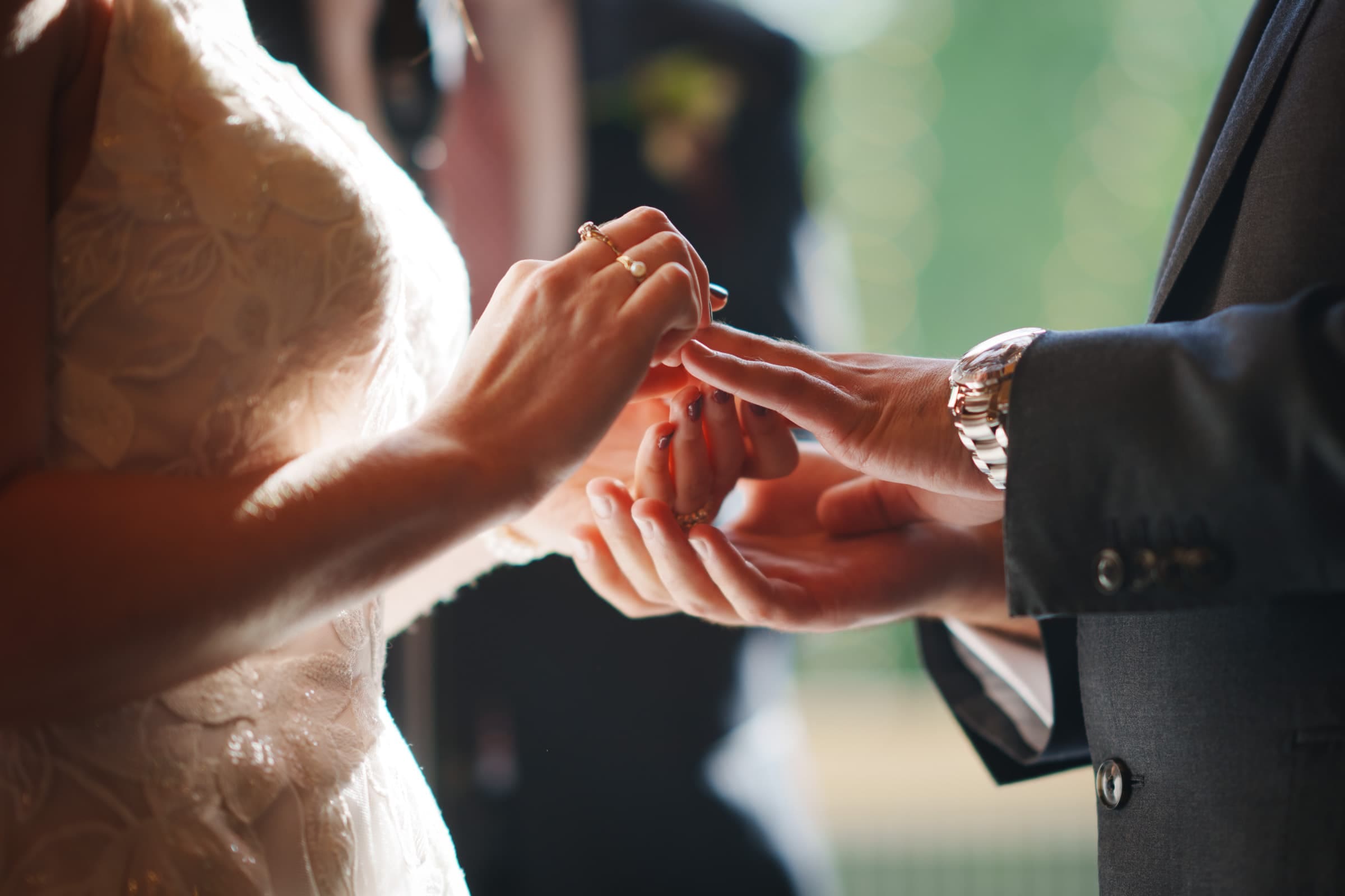 union grove farm wedding photography - kaylyn & jeremy A bride and groom exchange rings during a Union Grove Farm wedding. The bride's lace dress complements the groom’s dark suit and watch. This intimate moment is beautifully captured in close-up, with soft lighting creating a serene backdrop for their cherished union.
