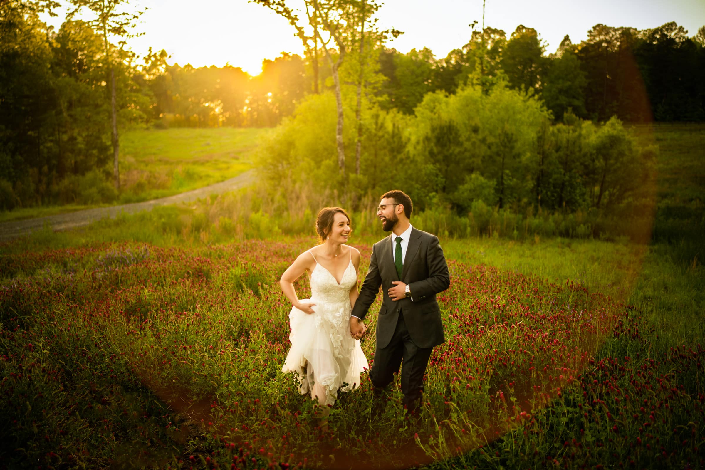union grove farm wedding photography - kaylyn & jeremy A couple in formal attire walks hand in hand through a lush, green field at sunset, captured perfectly by Union Grove Farm wedding photography. The woman is in a white dress, the man in a suit, as the warm glow of the sun creates an enchantingly romantic atmosphere.