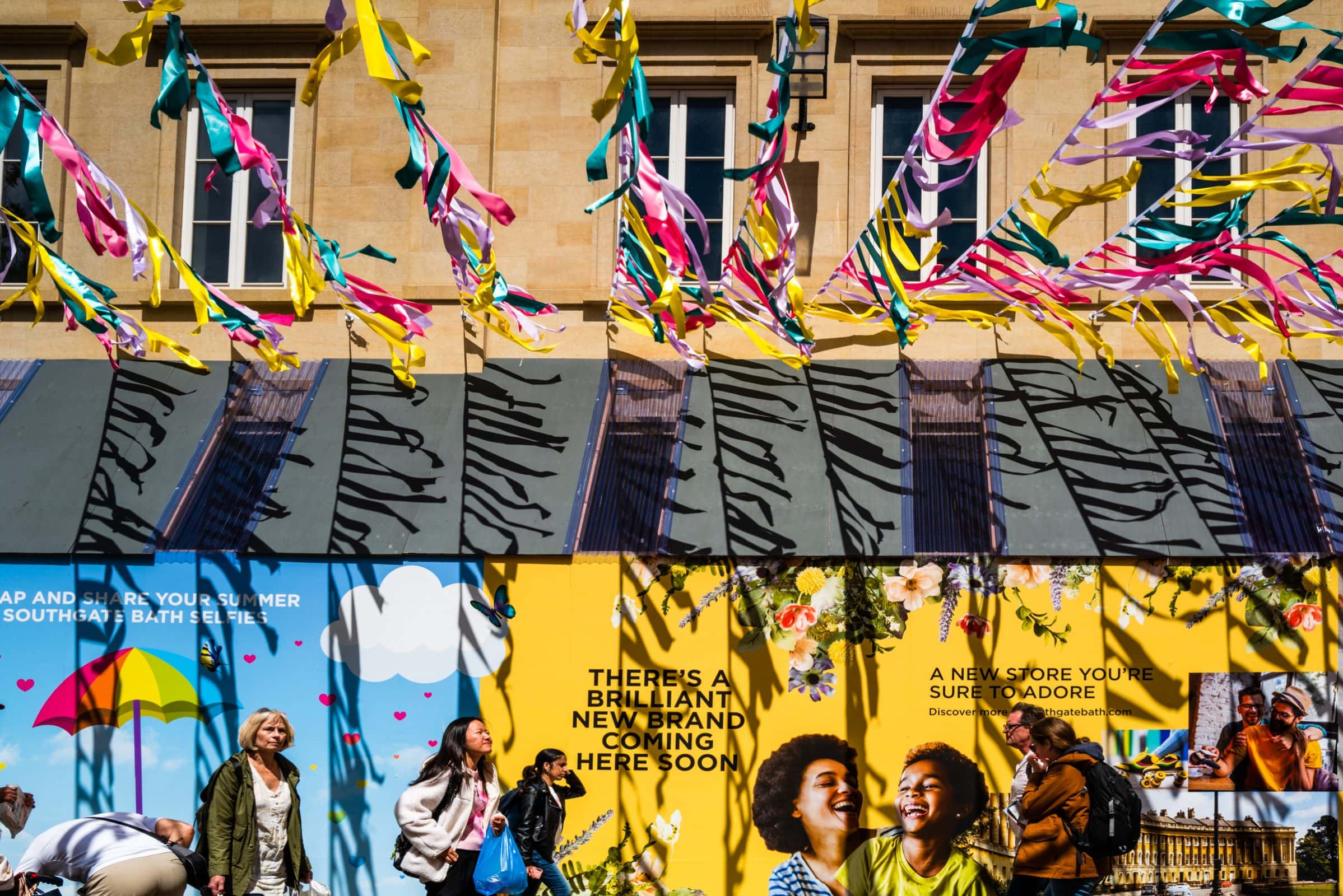 strengthening my photography skillset: a journey of self-development A colorful storefront with vibrant banners and streamers hanging above showcases the owner's photography skillset. The store windows display bright posters promoting a new brand. People pass by, enjoying the lively atmosphere and sunny weather.