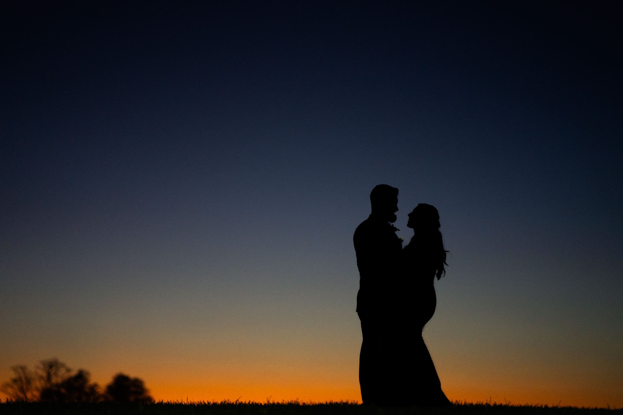 Silhouetted against a colorful dusk sky at Rose Hill Estate, a couple stands together, with the sunset creating a warm gradient from deep blue to orange.