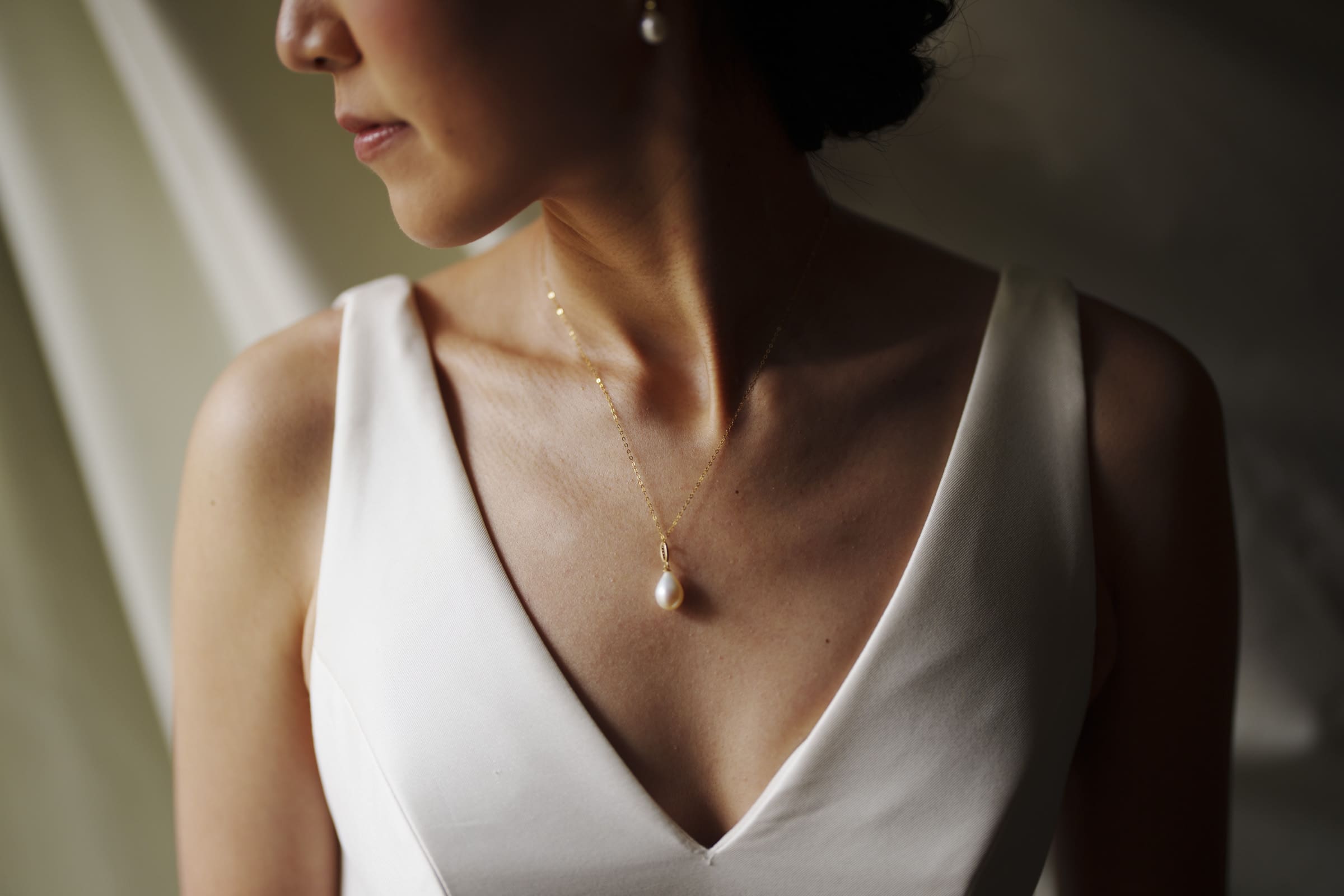 Carolina Inn Wedding - Frances & Lewis A woman in a white dress with a V-neckline, elegantly showcases her pearl necklace at the Carolina Inn. The background is softly blurred, capturing the essence of this beautiful wedding moment.