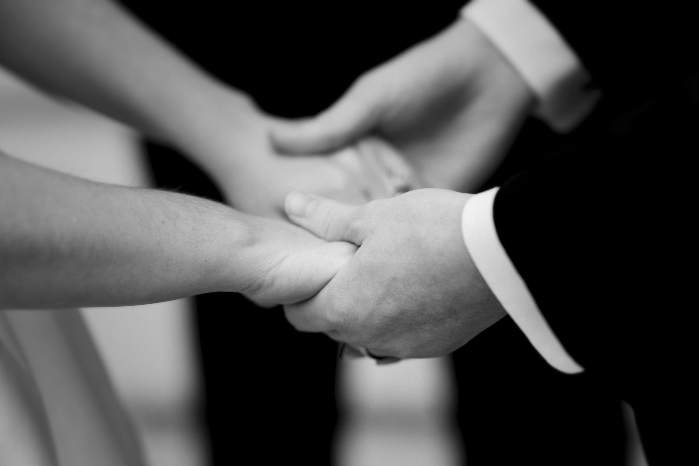 A black and white close-up image captures two people holding hands. Elegantly dressed, they exude an air of grace and anticipation, hinting at a special ceremony, perhaps an Umstead Hotel wedding.
