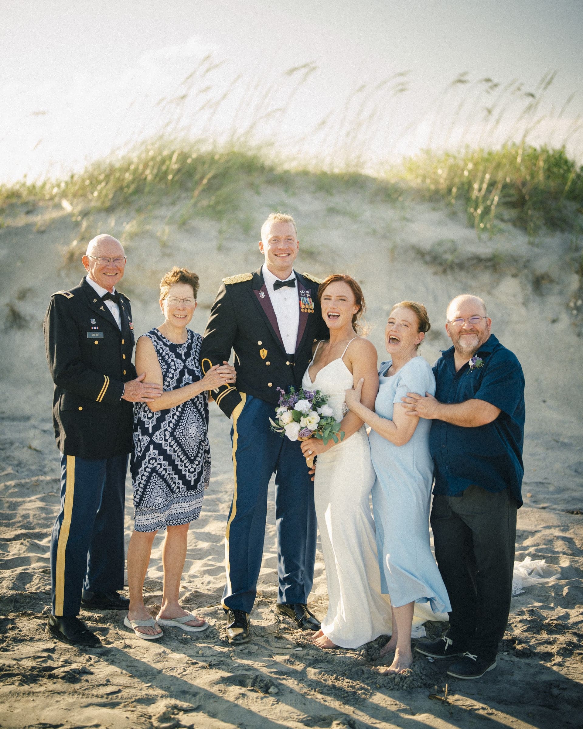 A joyful, candid family wedding portrait on the beach dunes at Topsail Beach, North Carolina, captured by wedding photographer Joe Payne.