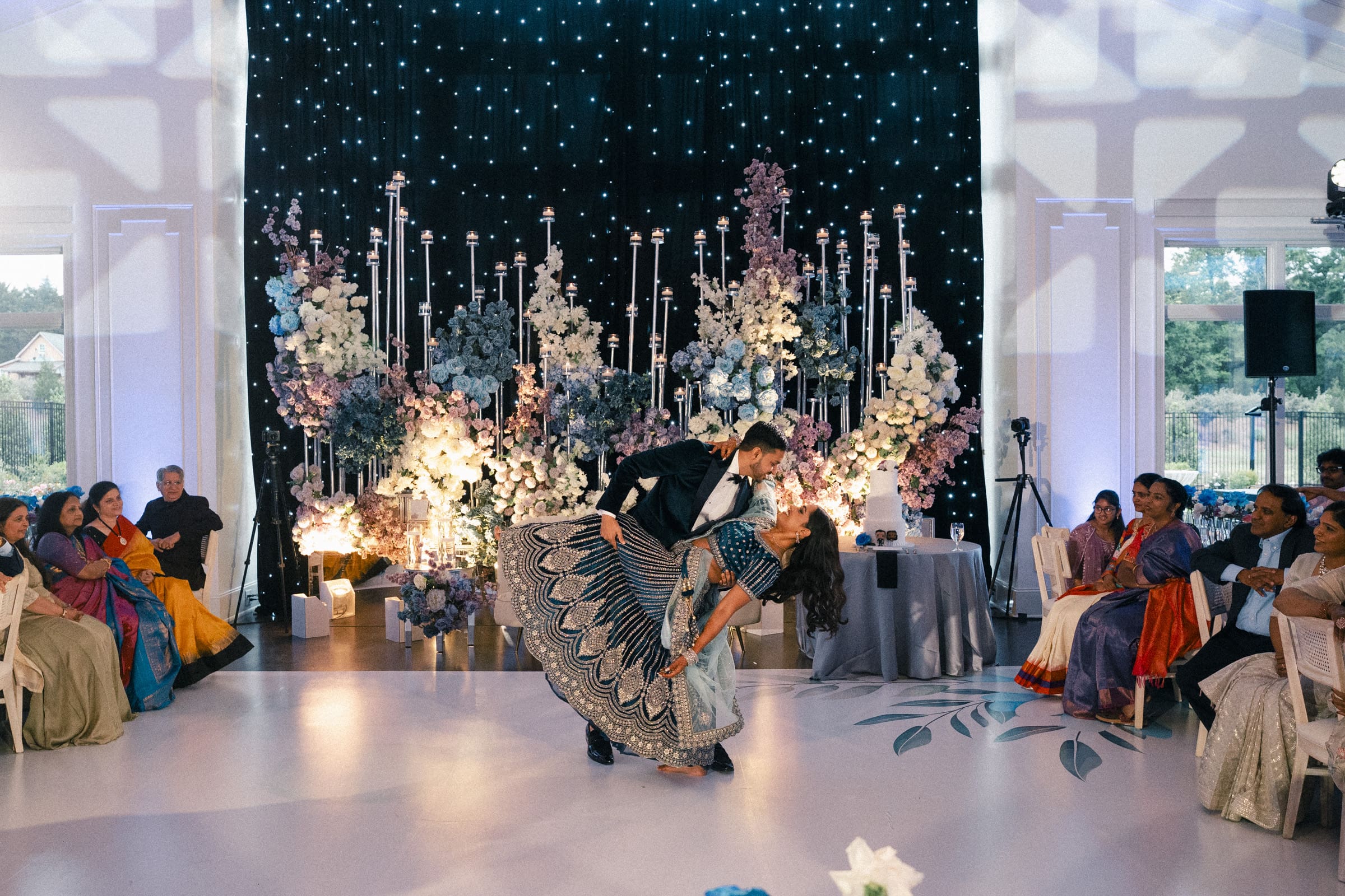 A groom dips his bride dramatically during their first dance on a stunning floral stage under a starry backdrop at Donovan Manor.