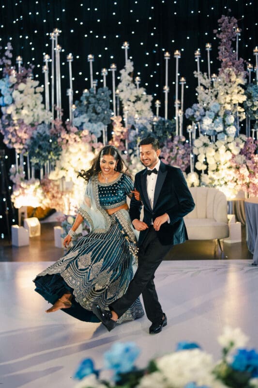 An Indian bride and groom share a beautiful, romantic dance together on a decorated stage during their evening wedding reception.