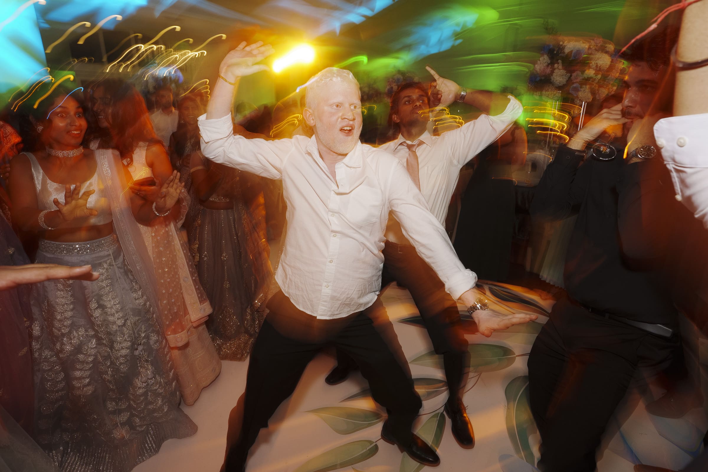 A wedding guest dances energetically under colorful, dynamic party lights during a lively reception celebration at Donovan Manor.