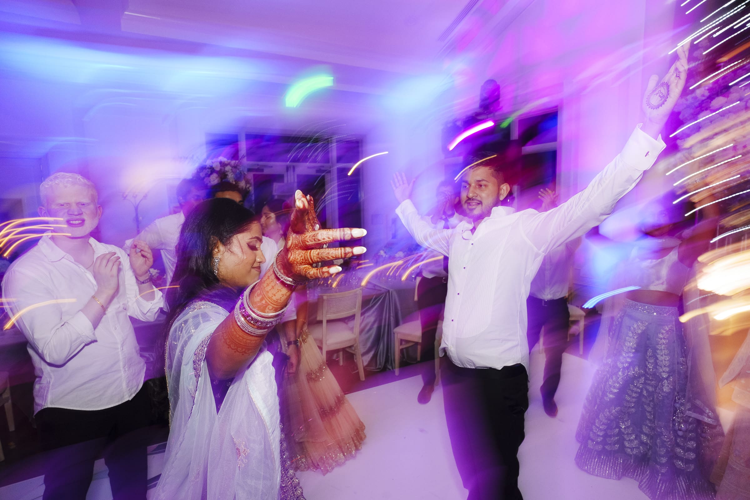 Wedding guests dance joyfully with the bride and grroom under colorful lights during the final party celebration of an Indian wedding reception at Donovan Manor.
