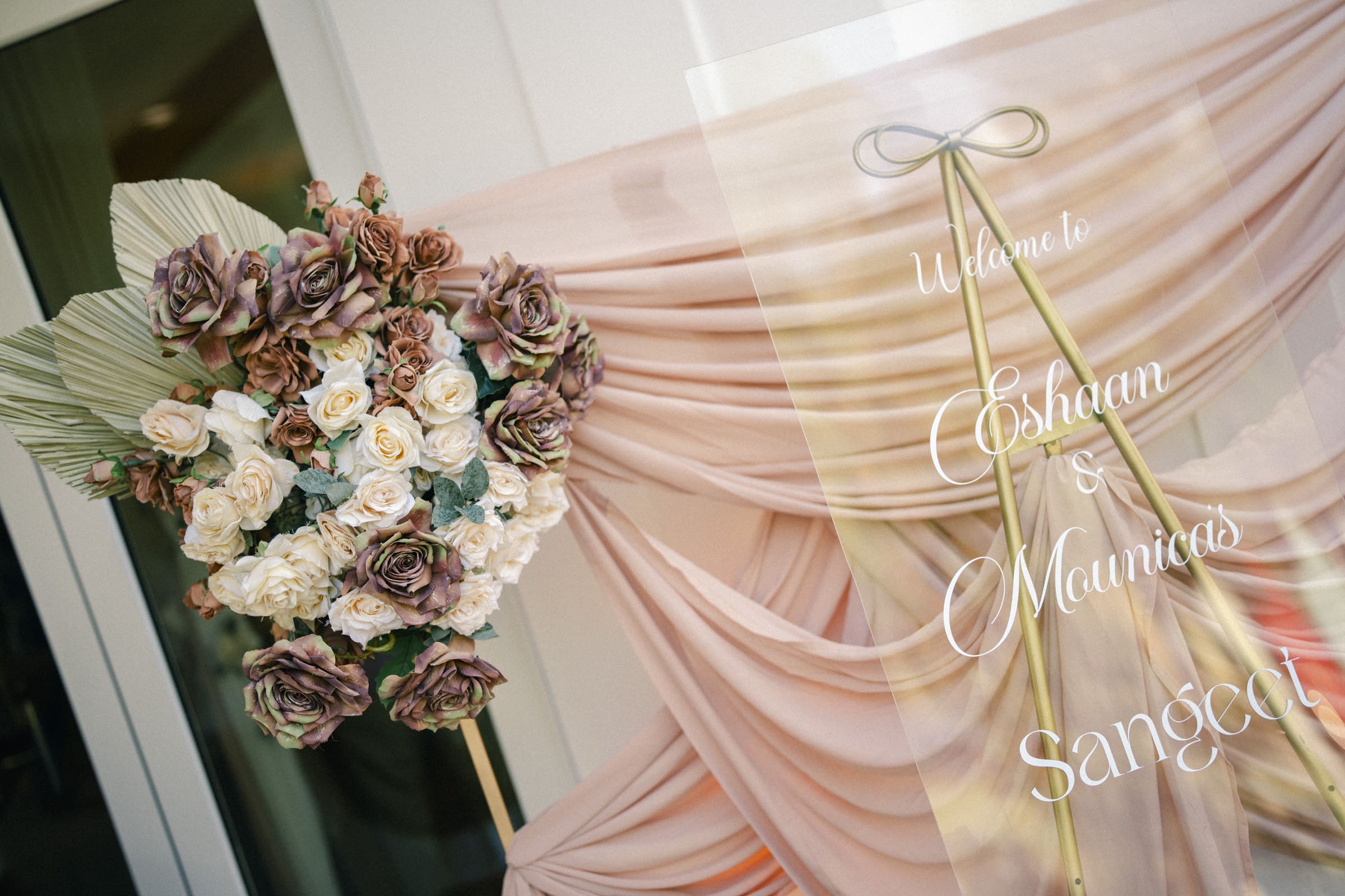 An elegant glass welcome sign with gold calligraphy for a Sangeet night, accented by white and mauve roses at a Raleigh Indian wedding by Joe Payne Photography.