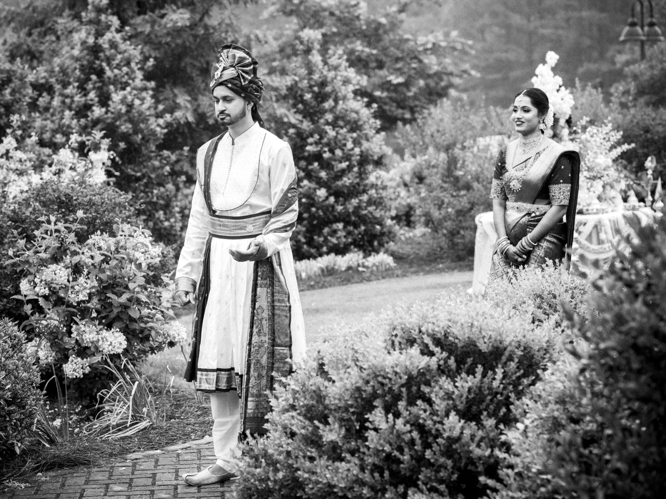 A timeless black and white wedding portrait of an Indian bride approaching her groom from behind for their first look at The Pavilion at Carriage Farm.