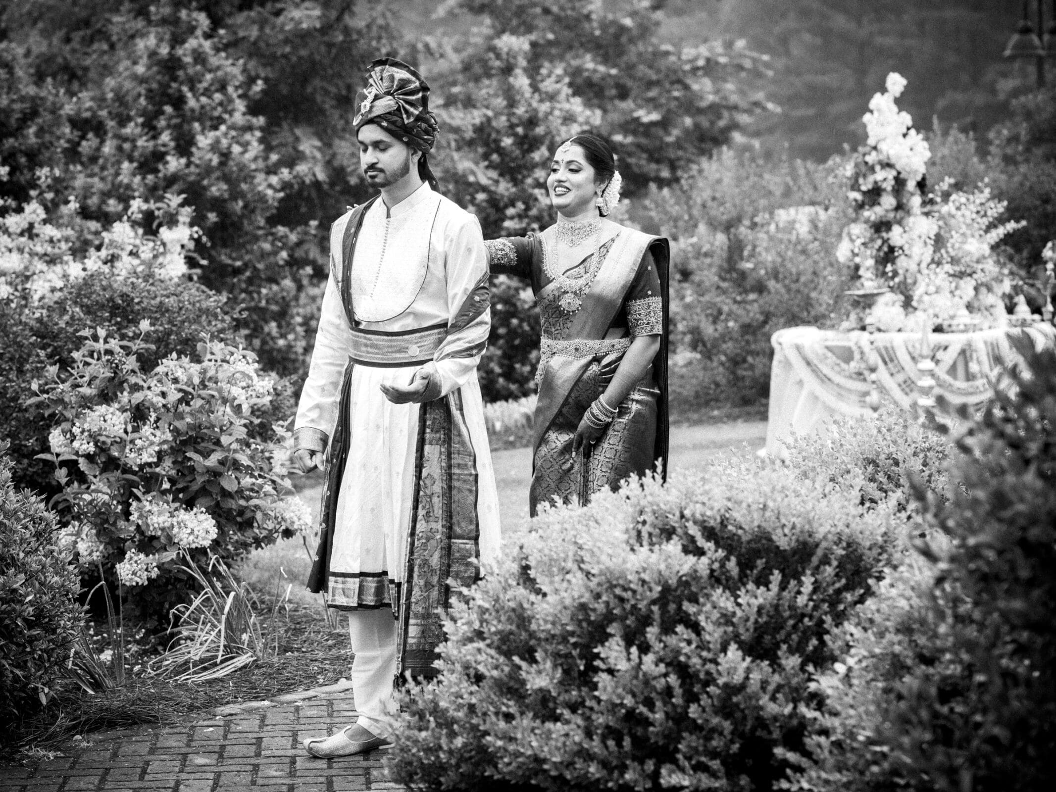 A candid black and white photo of an Indian bride tapping her groom on the shoulder during their first look reveal at The Pavilion at Carriage Farm.