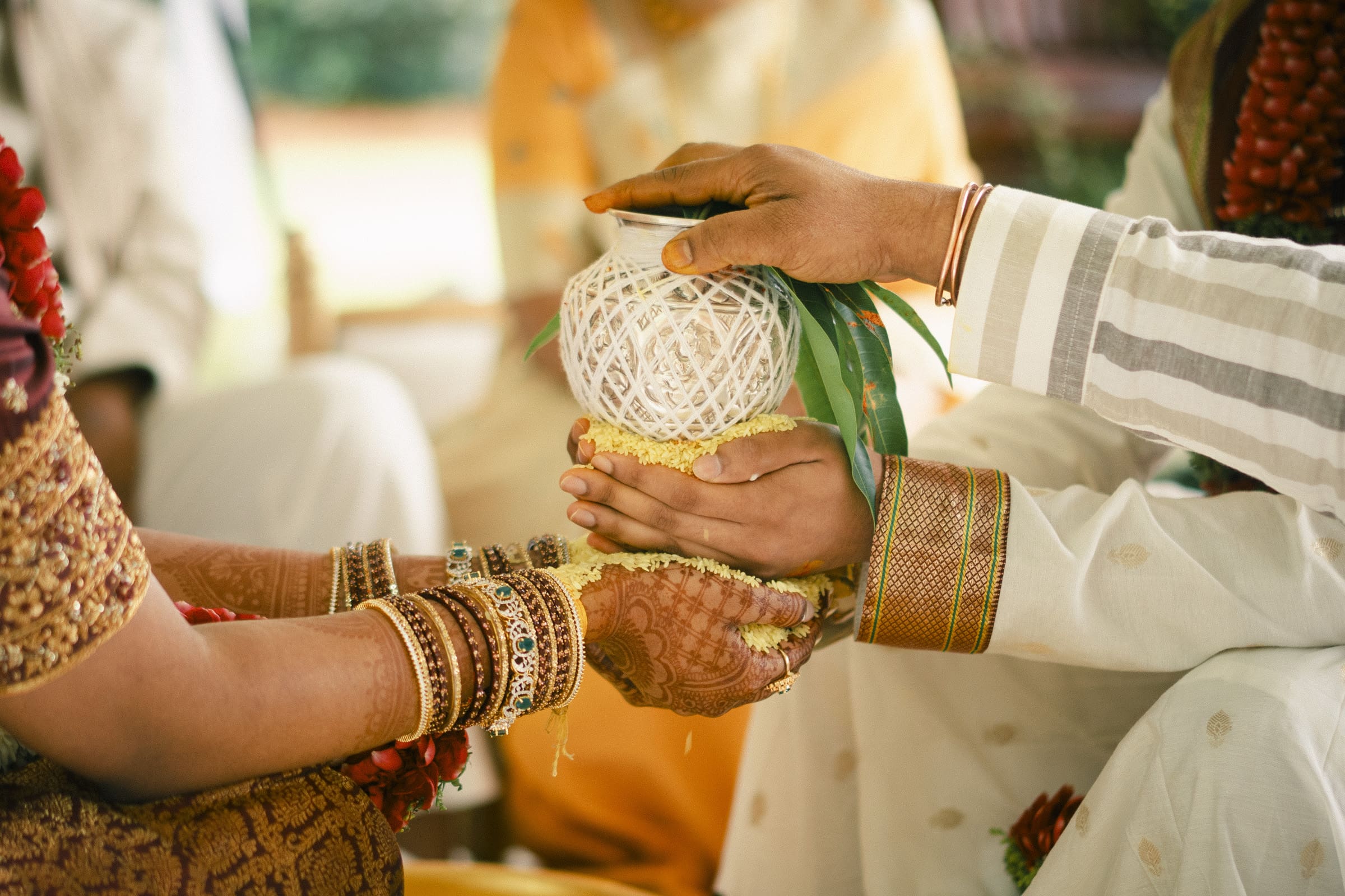 A macro detail shot of joined hands holding a ceremonial vessel during a traditional Hindu wedding ritual at The Pavilion at Carriage Farm.