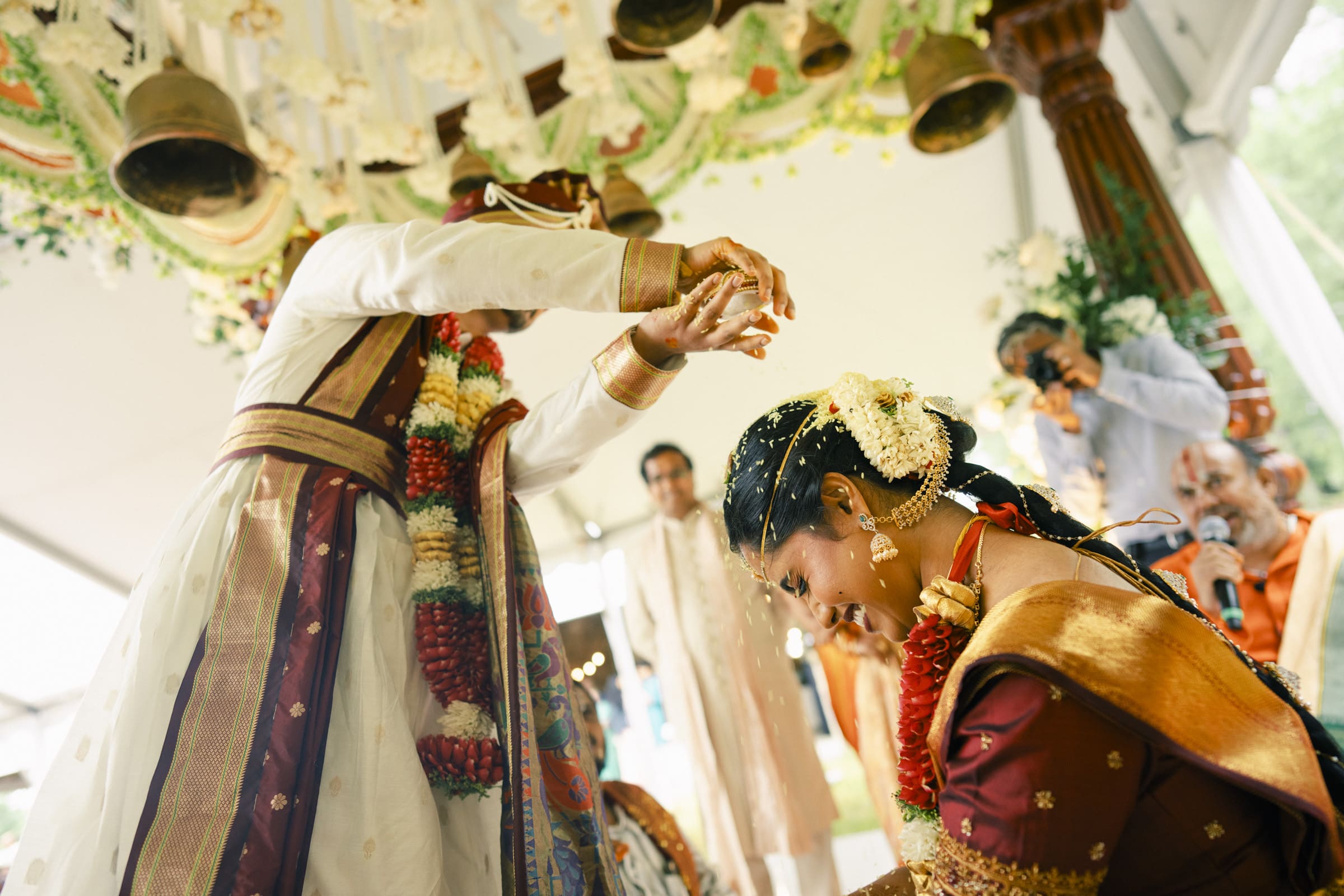 A groom pours sacred turmeric rice over his bride's head during the joyful Talambralu ritual at a Carriage Farm Indian wedding.