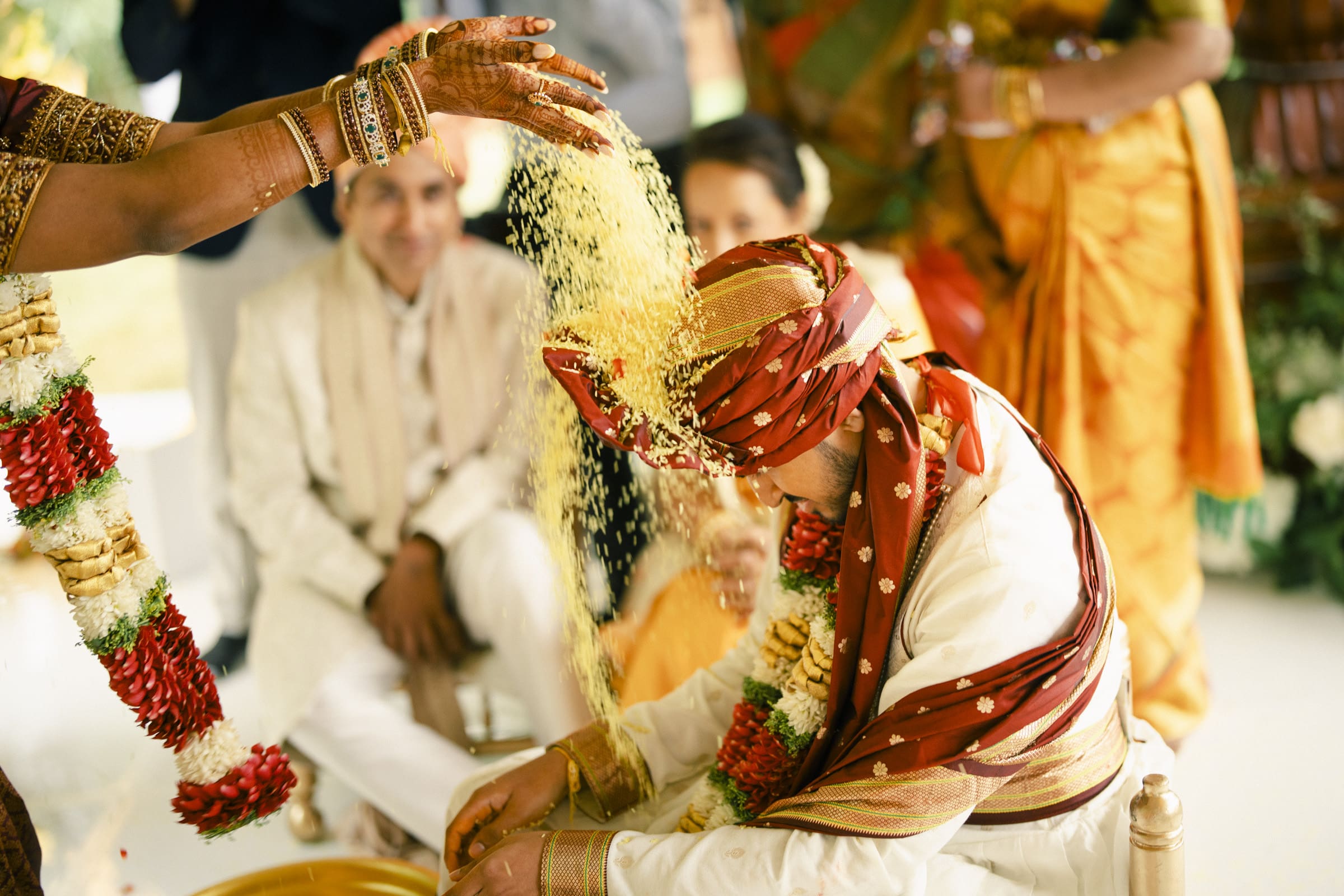 A dynamic close-up photograph of the sacred rice shower ritual at a traditional South Indian wedding ceremony.
