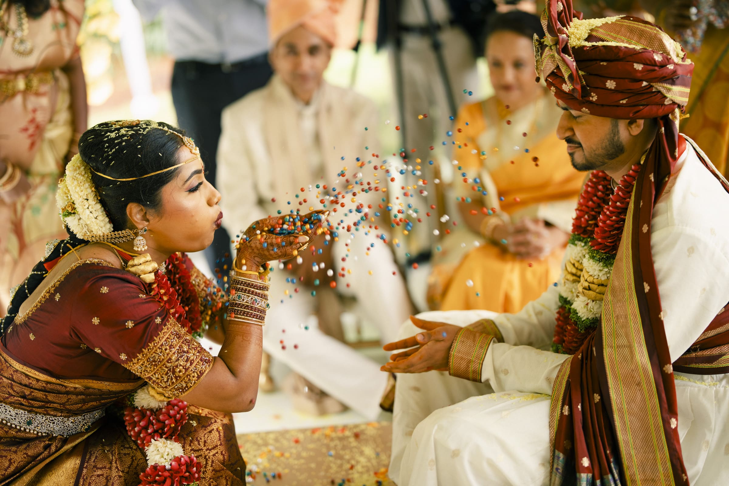 A playful bride blows colorful confetti toward her groom during their wedding ceremony at The Pavilion at Carriage Farm by Joe Payne Photography.