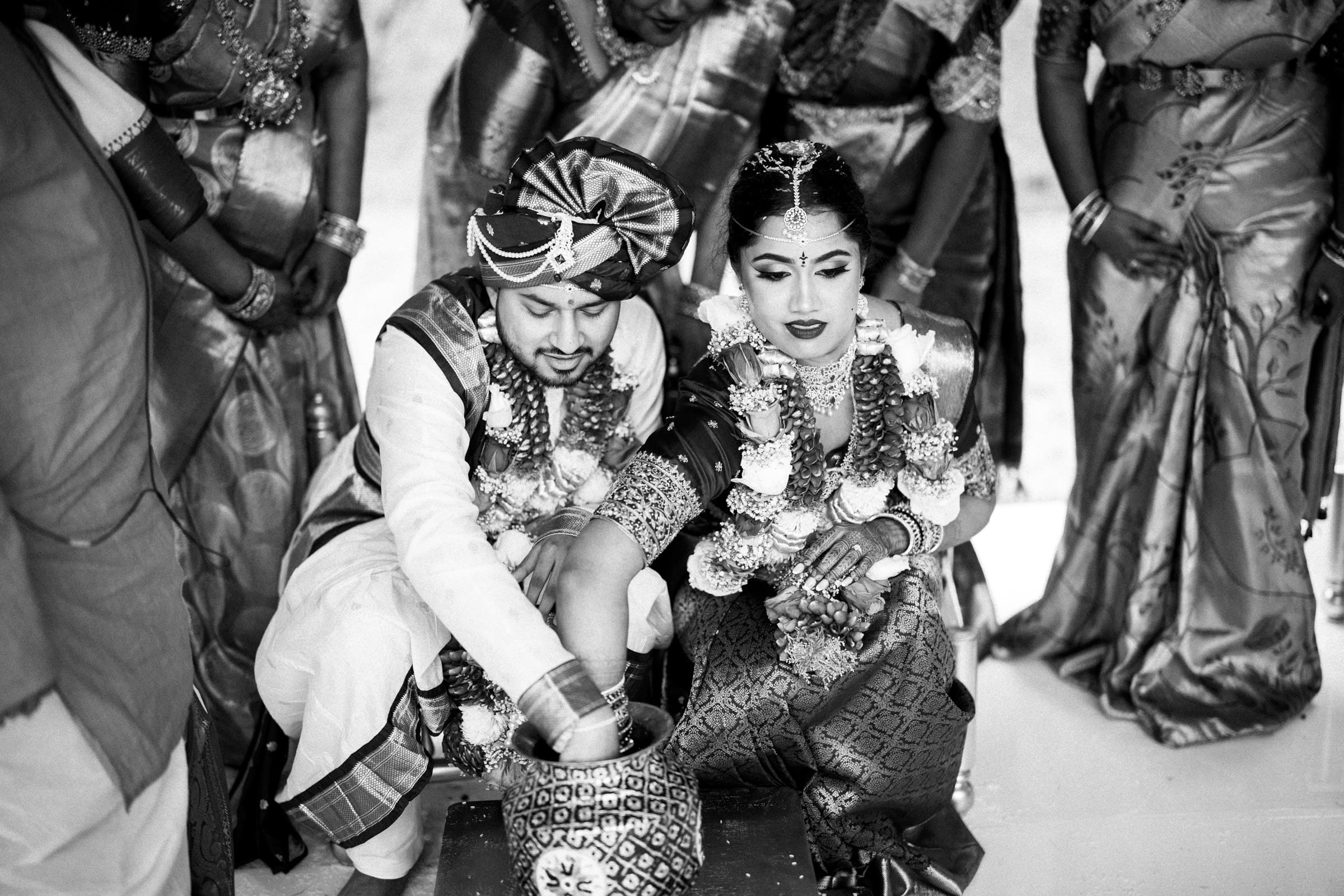 A black and white candid photo of a bride and groom playing the traditional wedding ring game in a decorated vessel at Carriage Farm.