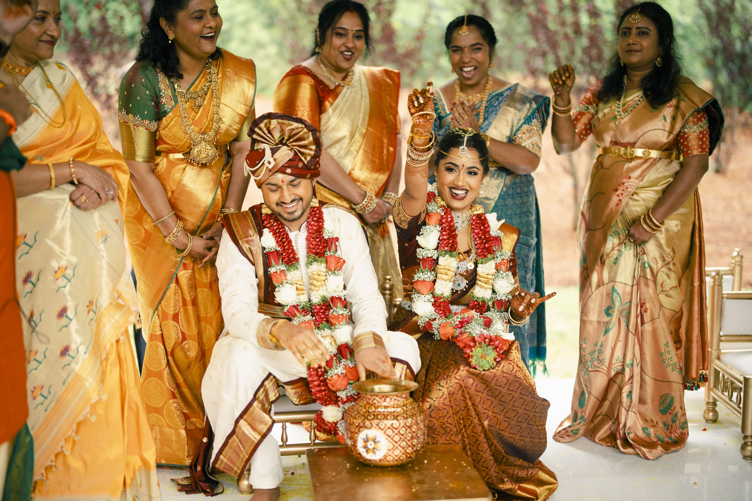 A laughing bride and groom celebrate with family during their mandap rituals at a vibrant Pavilion at Carriage Farm Indian wedding, photographed by Joe Payne Photography.