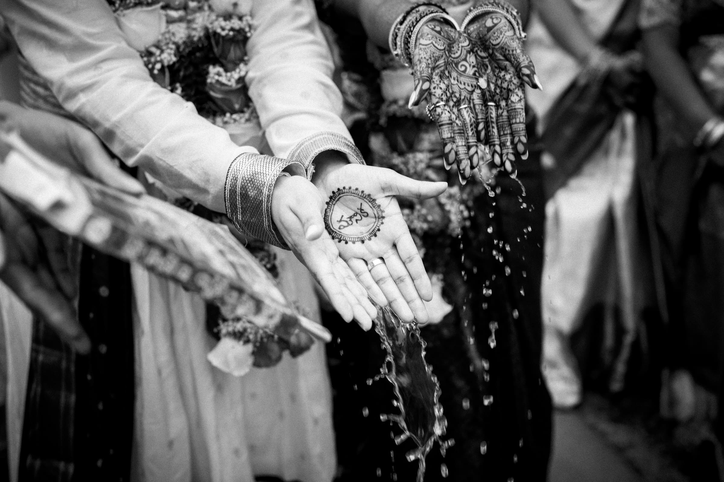 A black and white detail photo of a sacred water-pouring blessing ritual during a Hindu wedding ceremony at The Pavilion at Carriage Farm.