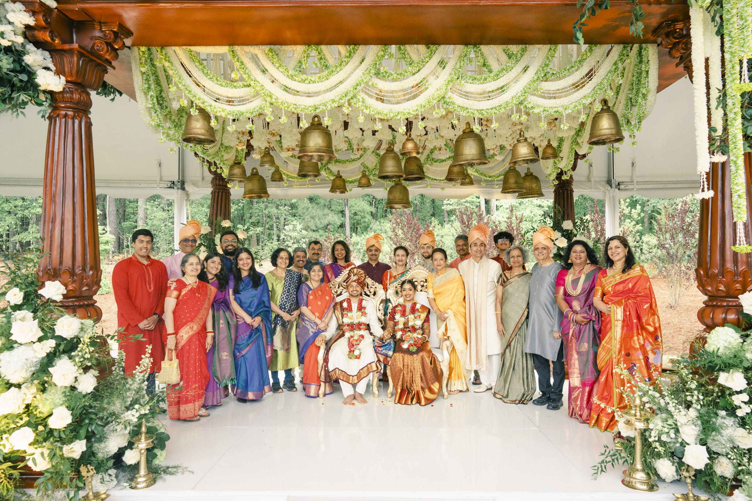 Wedding guests and family members pose with the bride and groom under the floral mandap canopy at a Carriage Farm Indian wedding celebration.