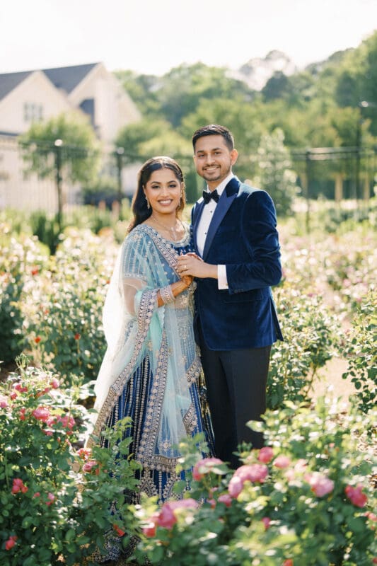 A traditional wedding portrait of an Indian bride and groom smiling at the camera in a blooming rose garden at Donovan Manor.