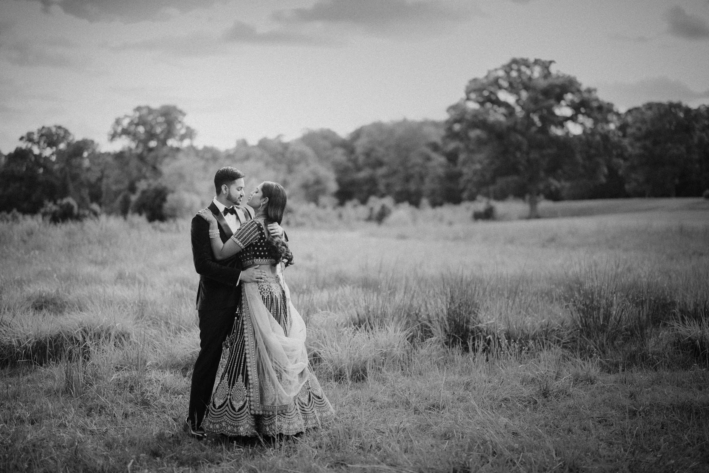A dramatic black and white wedding portrait of a bride and groom embracing intimately in a field under a cloudy sky at Donovan Manor.