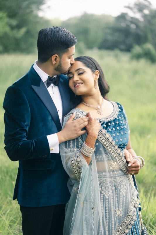 A groom tenderly kisses his bride's forehead during their outdoor reception portrait session at Donovan Manor.