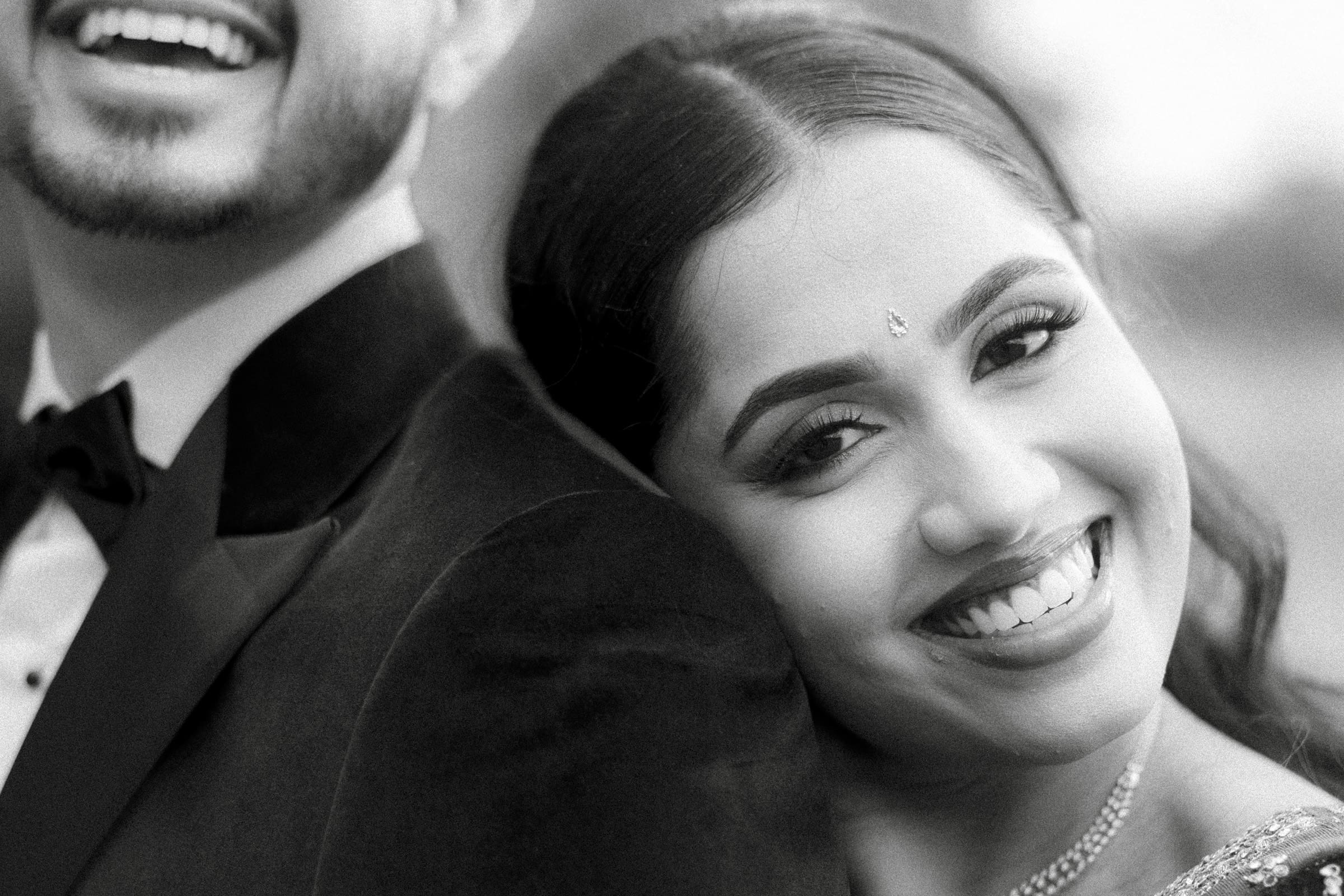 A classic black and white portrait capturing a candid, affectionate moment as the bride rests her head on the groom's shoulder.