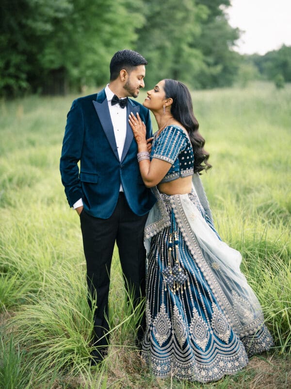 An elegant close-up portrait of an Indian bride in an embellished blue lehenga leaning against her groom's navy velvet tuxedo at Donovan Manor.