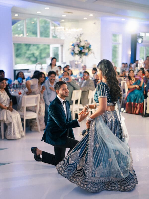 A groom playfully gets down on one knee for his bride during their wedding reception celebration inside Donovan Manor.