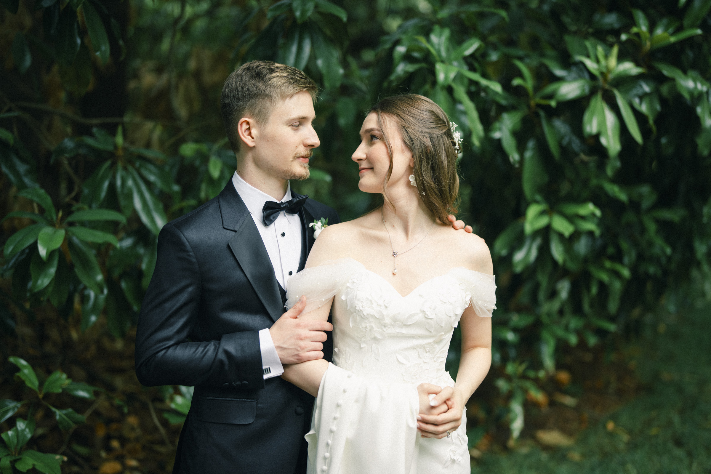 A bride and groom stand together outdoors at their Carolina Inn Wedding in Chapel Hill, dressed in formal wedding attire, gazing at each other with greenery in the background—an elegant spring celebration to remember. By award-winning Raleigh wedding photographer, Joe Payne.