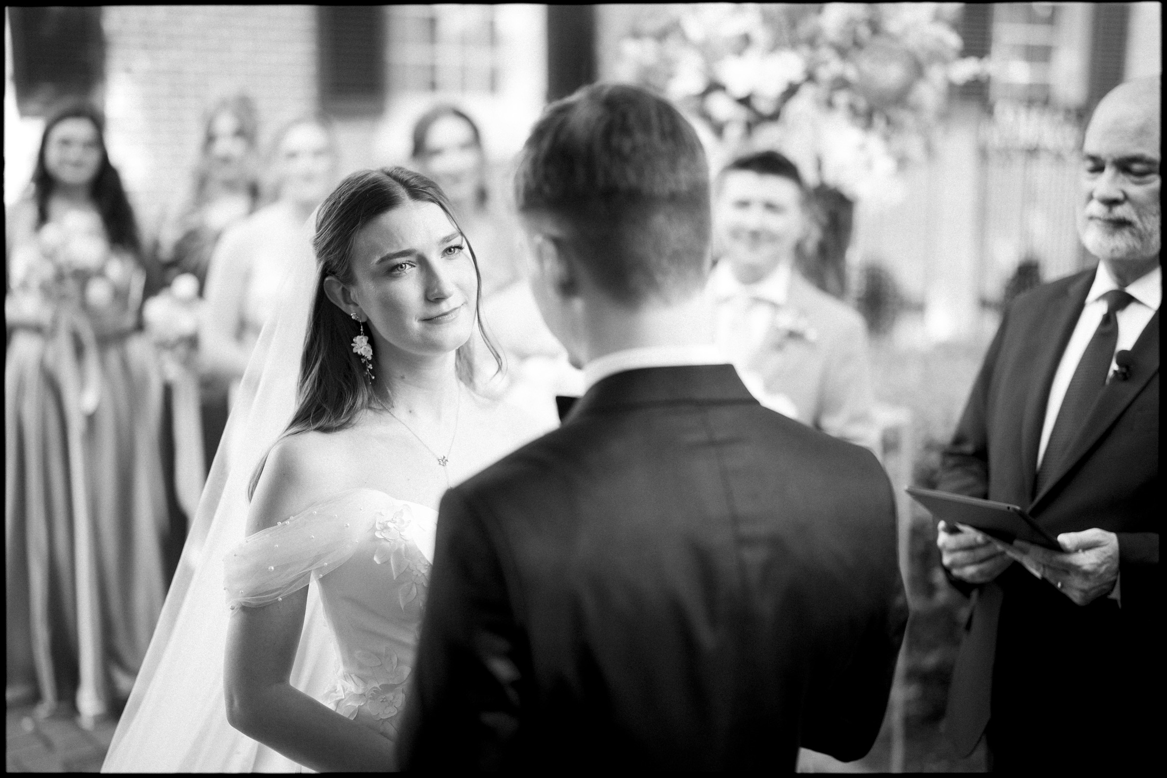 A bride in a wedding dress gazes emotionally at the groom during an elegant spring wedding ceremony at the Carolina Inn, with bridesmaids, a groomsman, and an officiant standing nearby. By award-winning Raleigh wedding photographer, Joe Payne.