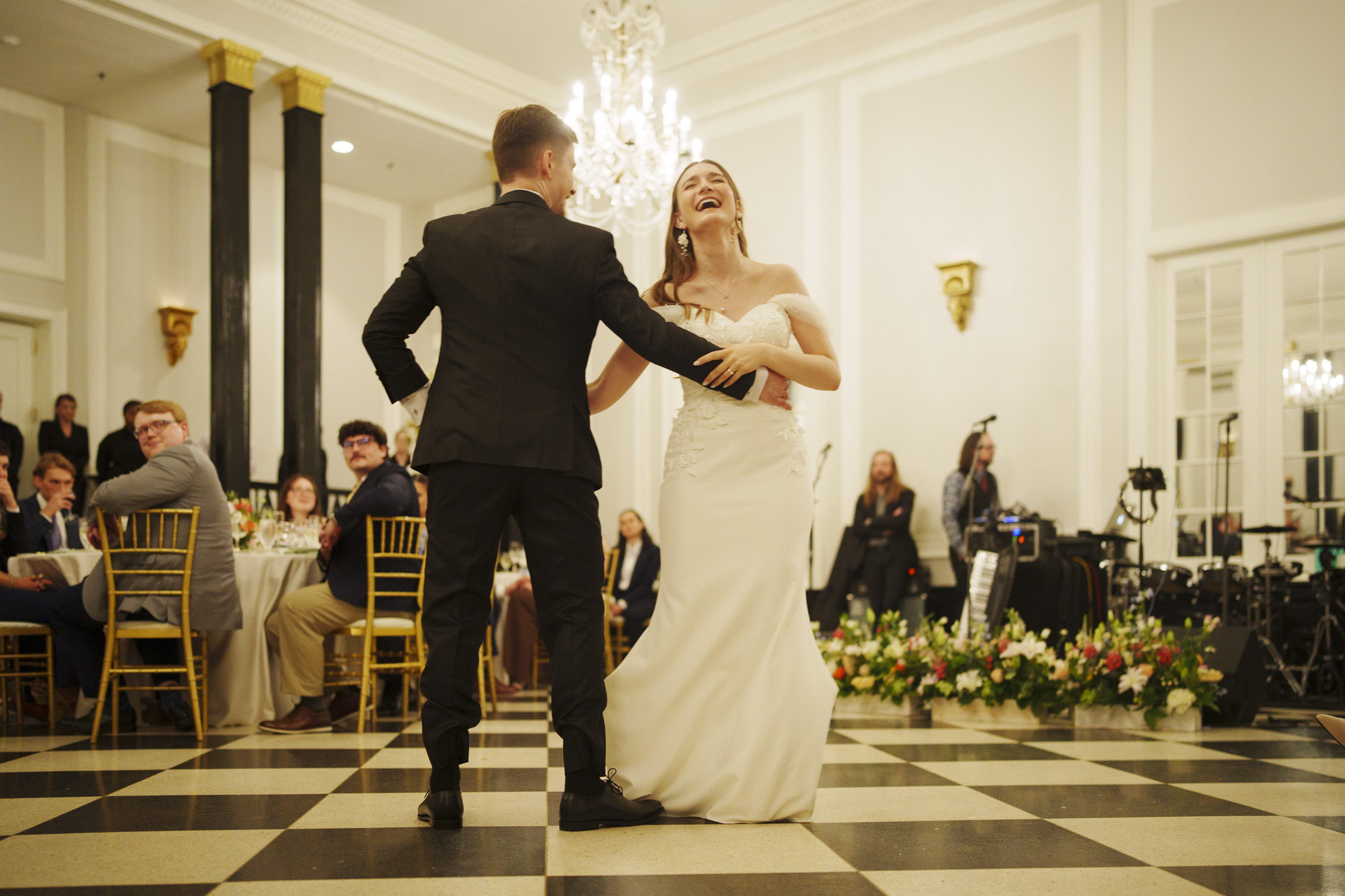 A bride and groom share a joyous first dance in a grand ballroom at their Carolina Inn Wedding in Chapel Hill, surrounded by seated guests and elegant décor, including chandeliers and floral arrangements—an unforgettable elegant spring celebration. By award-winning Raleigh wedding photographer, Joe Payne.
