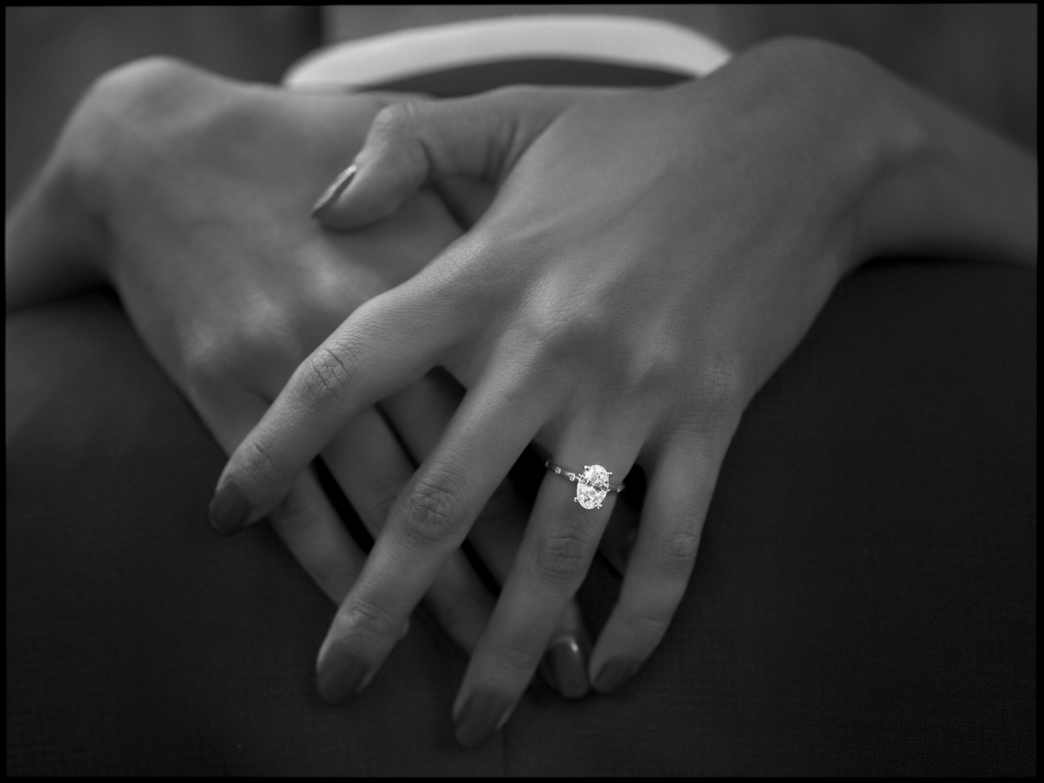 Close-up black and white engagement photography of hands clasped together, featuring an oval-cut diamond engagement ring on the ring finger. By award-winning Raleigh wedding photographer, Joe Payne.