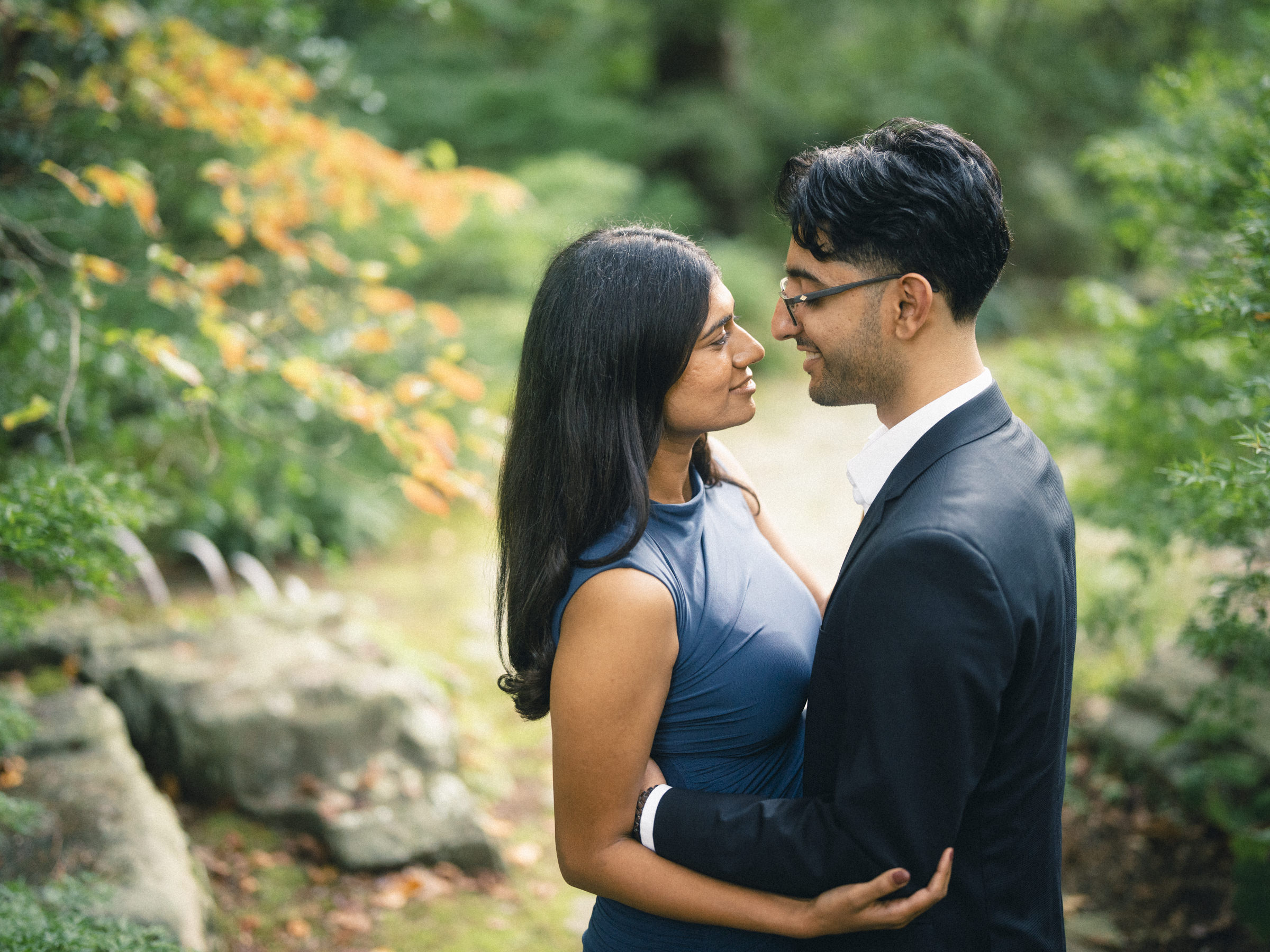 A couple in formal attire stands in a garden gazing at each other during an engagement photography session. By award-winning Raleigh wedding photographer, Joe Payne.