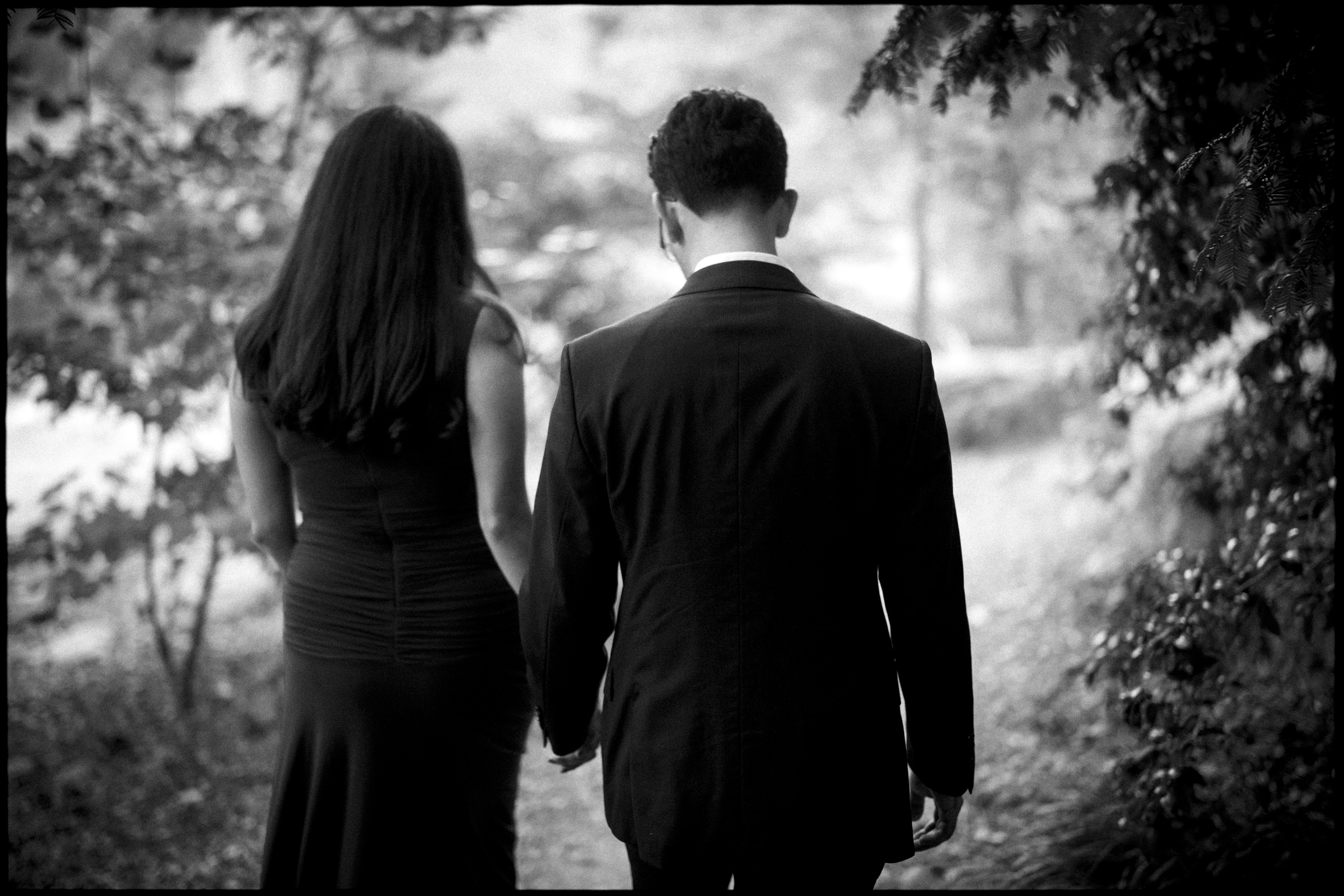 A couple holds hands while walking away from the camera on a wooded path during an engagement photography session at Duke Gardens. By award-winning Raleigh wedding photographer, Joe Payne.